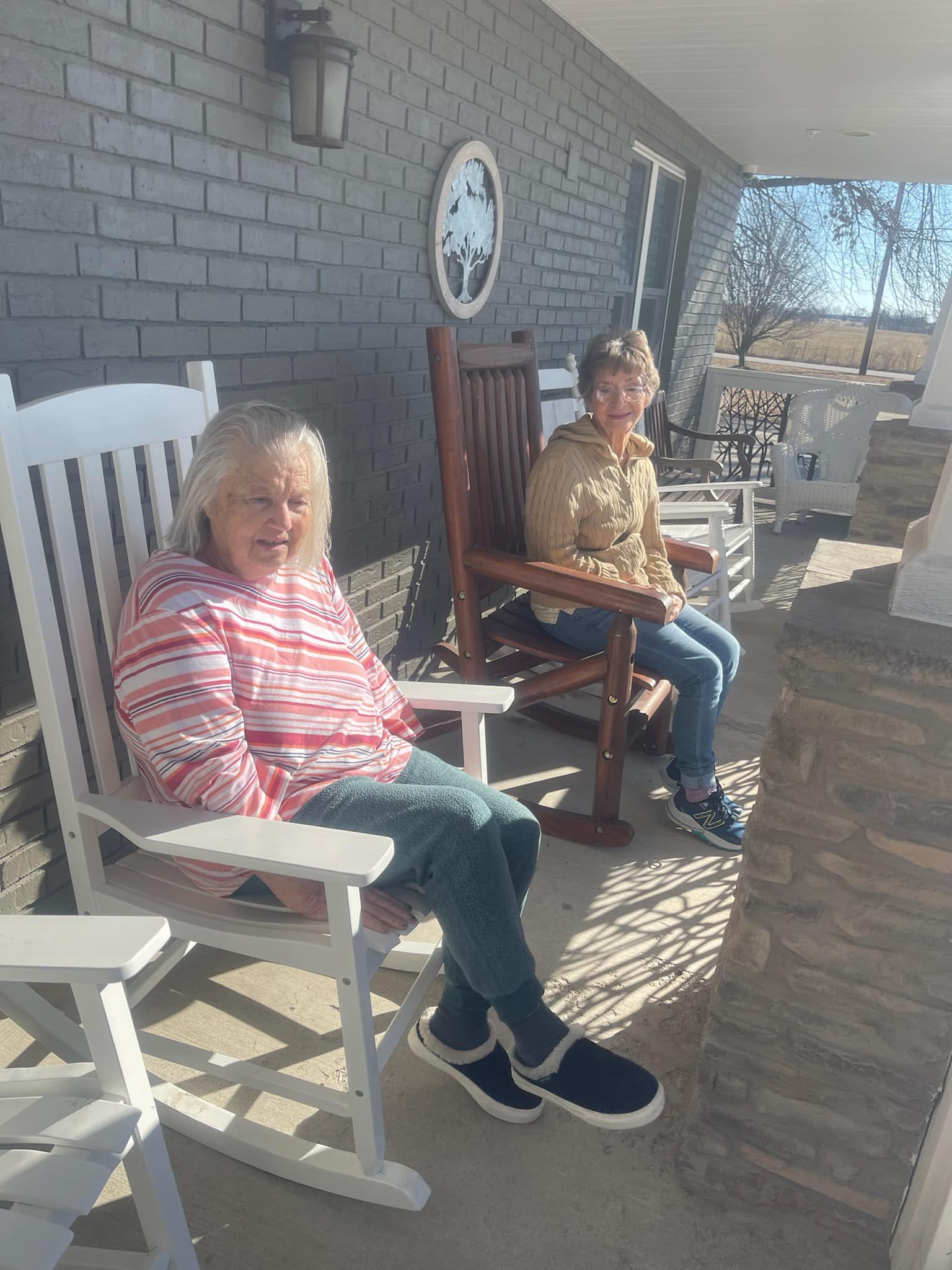 Two women are sitting in rocking chairs on a porch.
