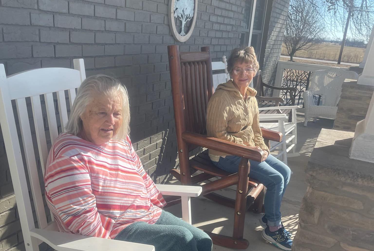 Two women are sitting in rocking chairs on a porch.