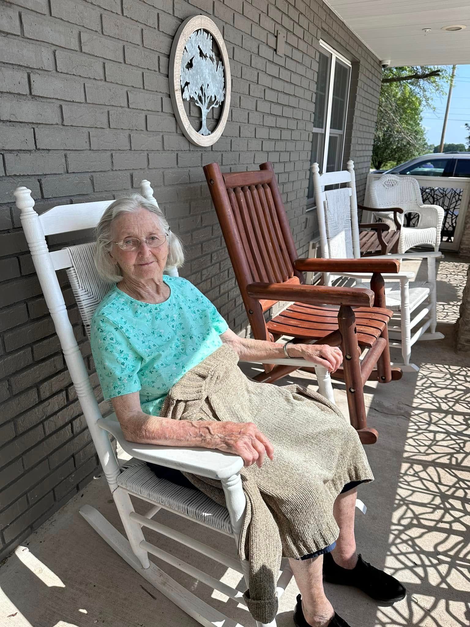 An elderly woman is sitting in a rocking chair on a porch.