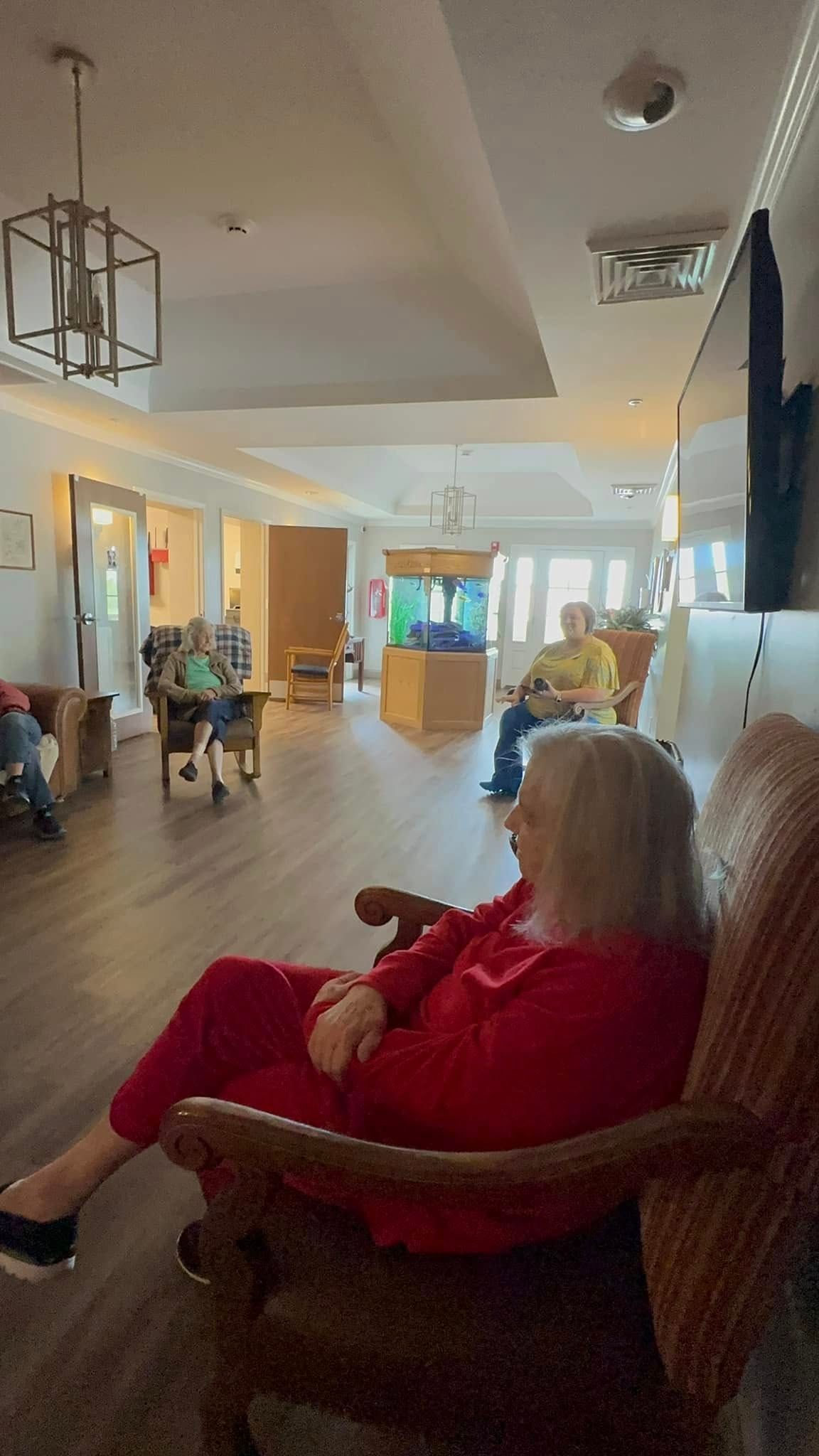 A woman in a red sweater is sitting in a chair in a living room.