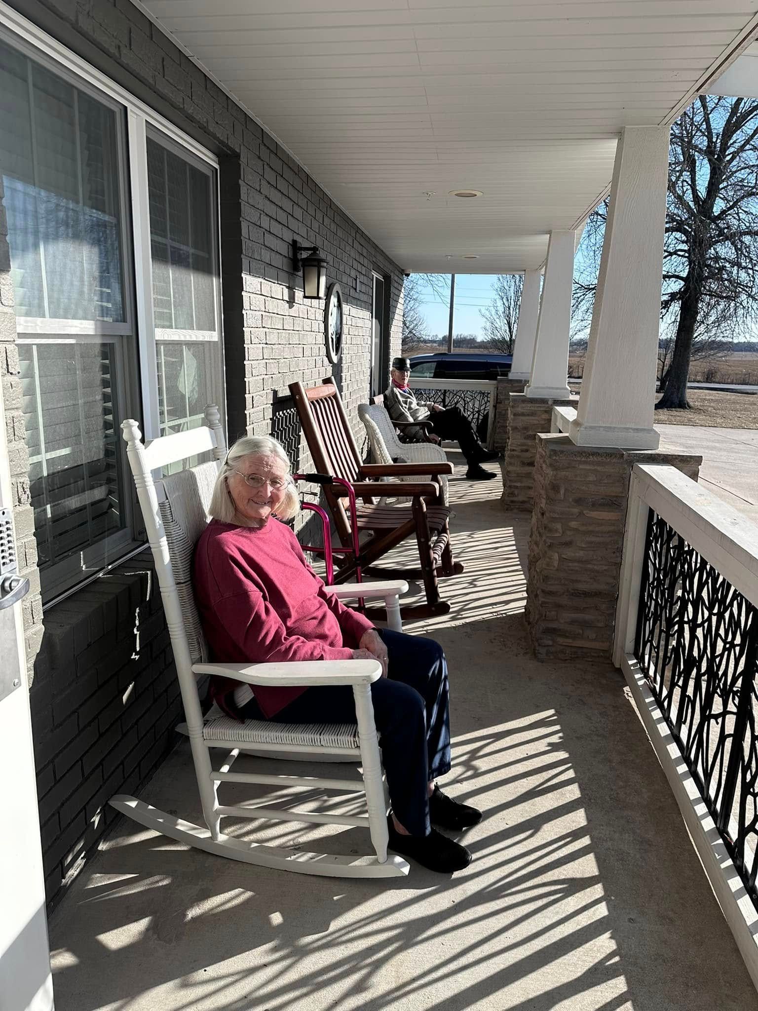 An elderly woman is sitting in a rocking chair on a porch.