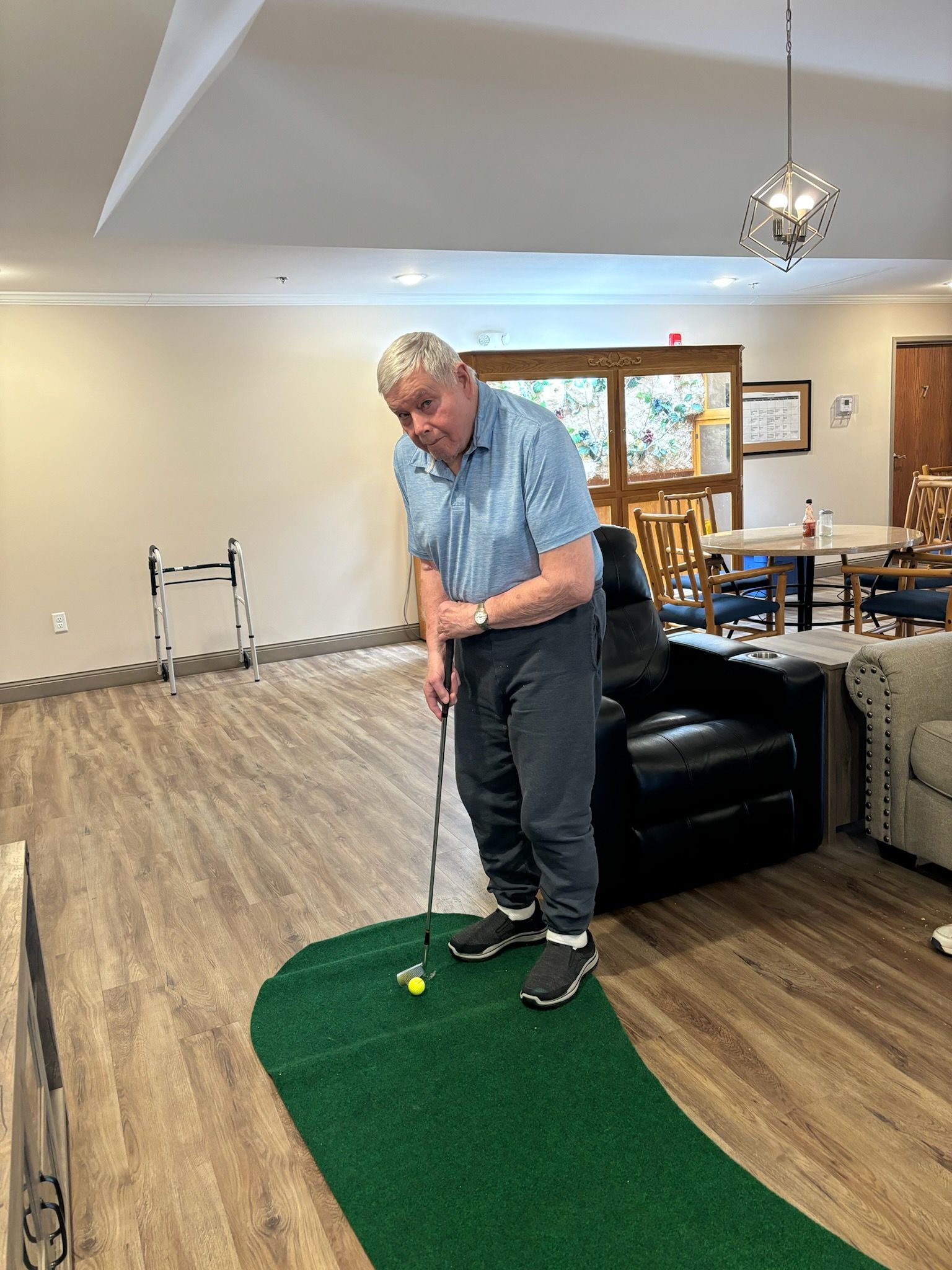 A man is playing golf on a green mat in a living room.