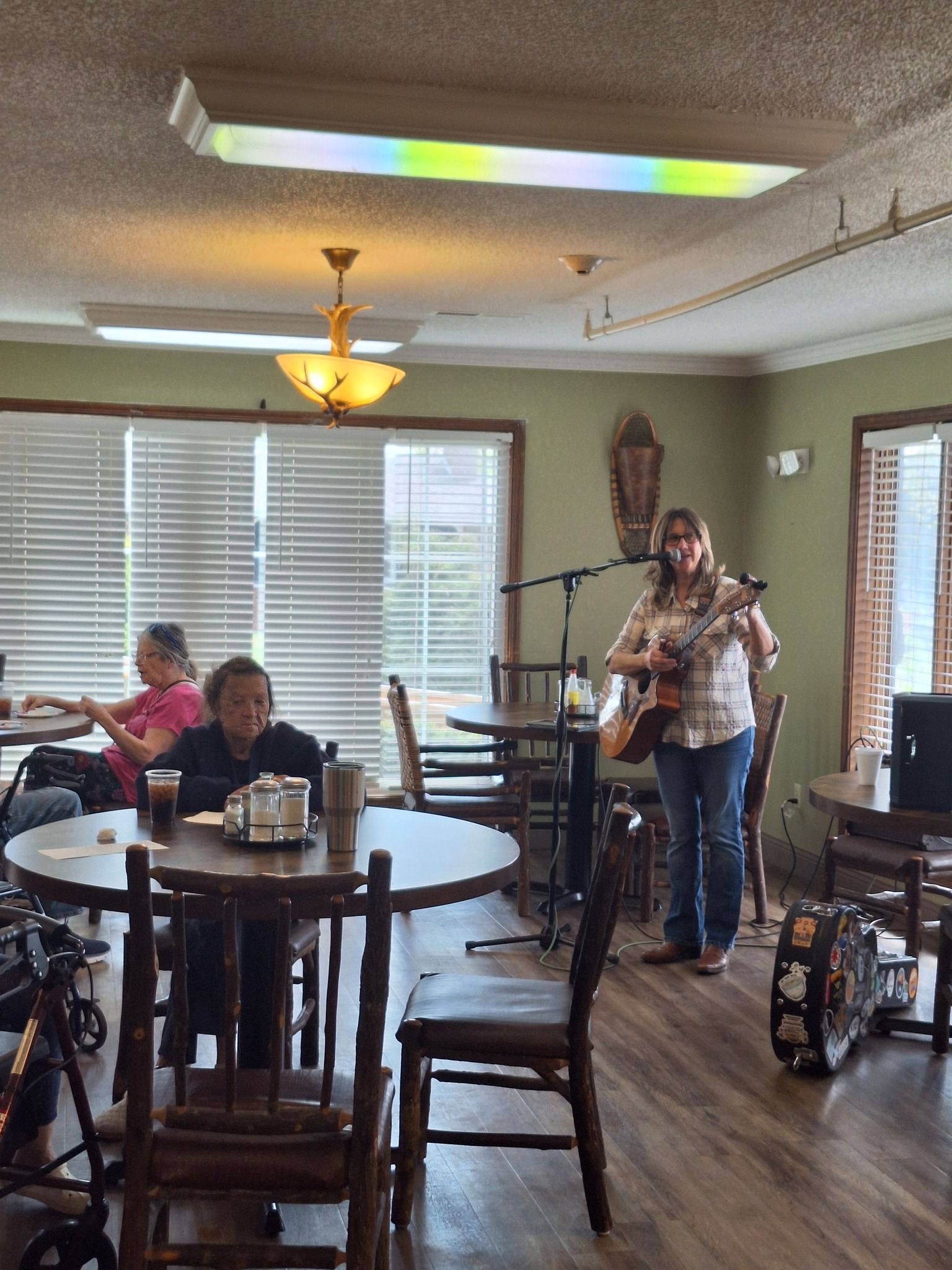 A woman is playing a guitar in a restaurant while people sit at tables.