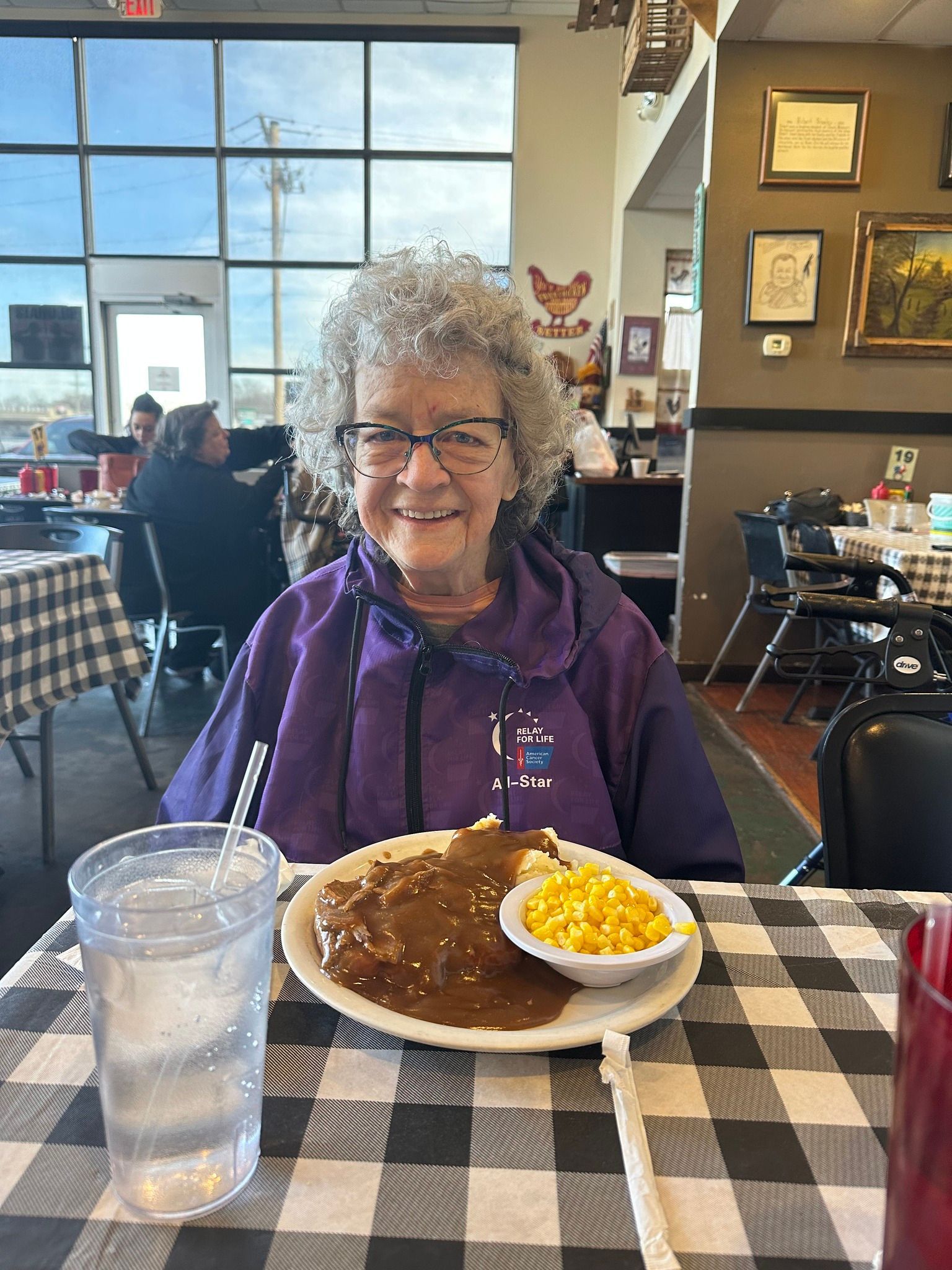 An elderly woman is sitting at a table with a plate of food.