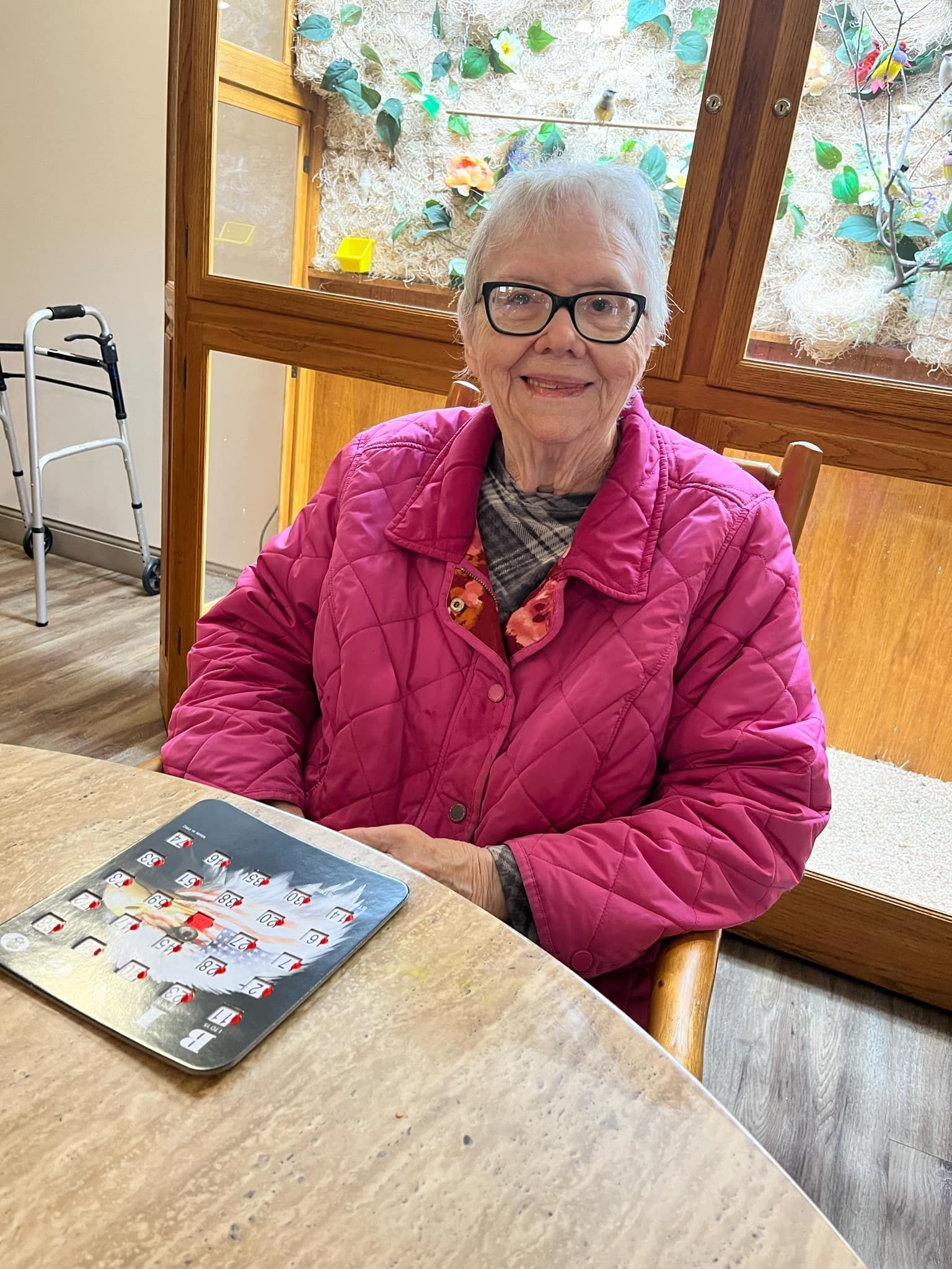 An elderly woman is sitting at a table with a book on it.