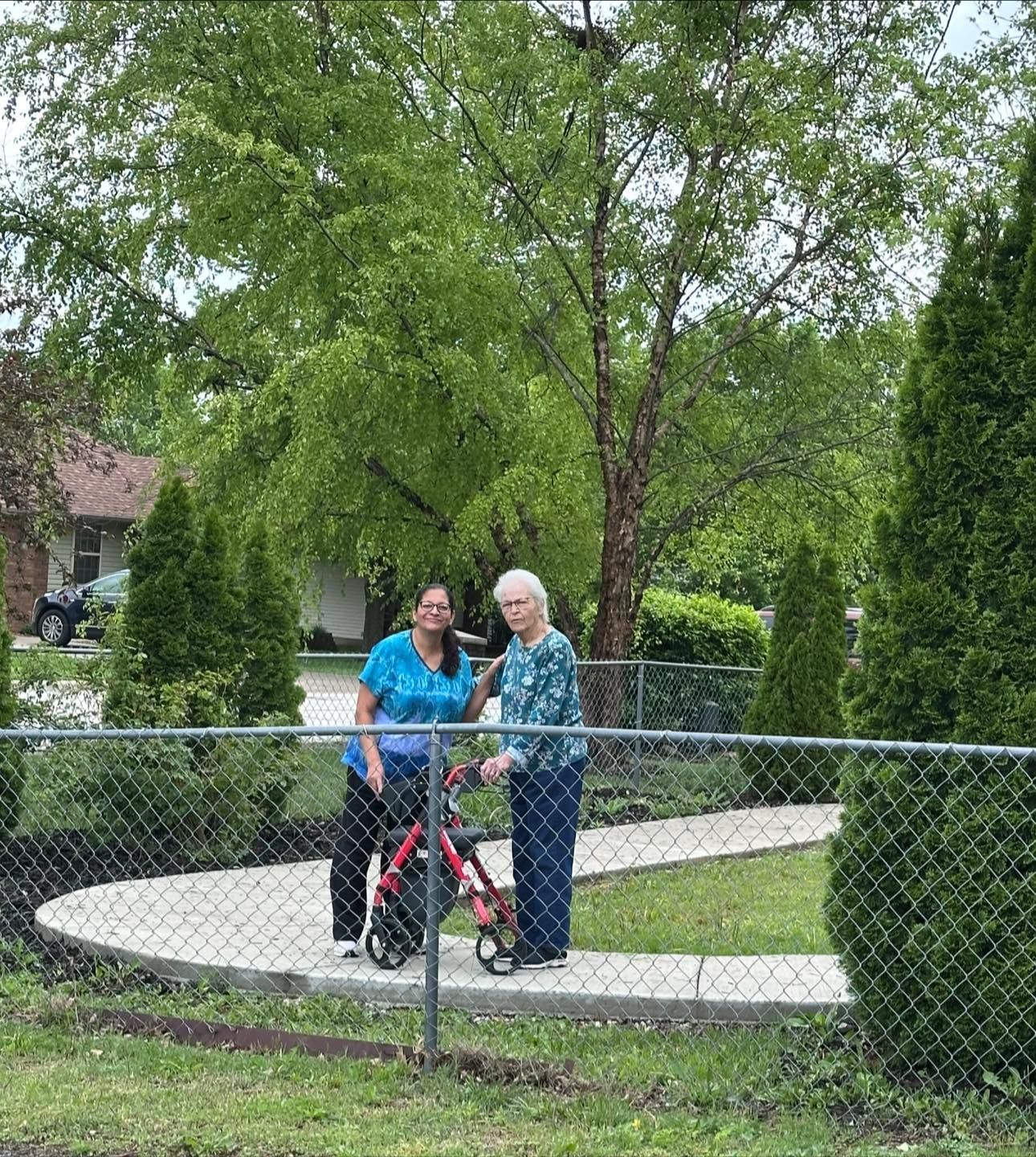 Two women are standing next to each other in front of a chain link fence.