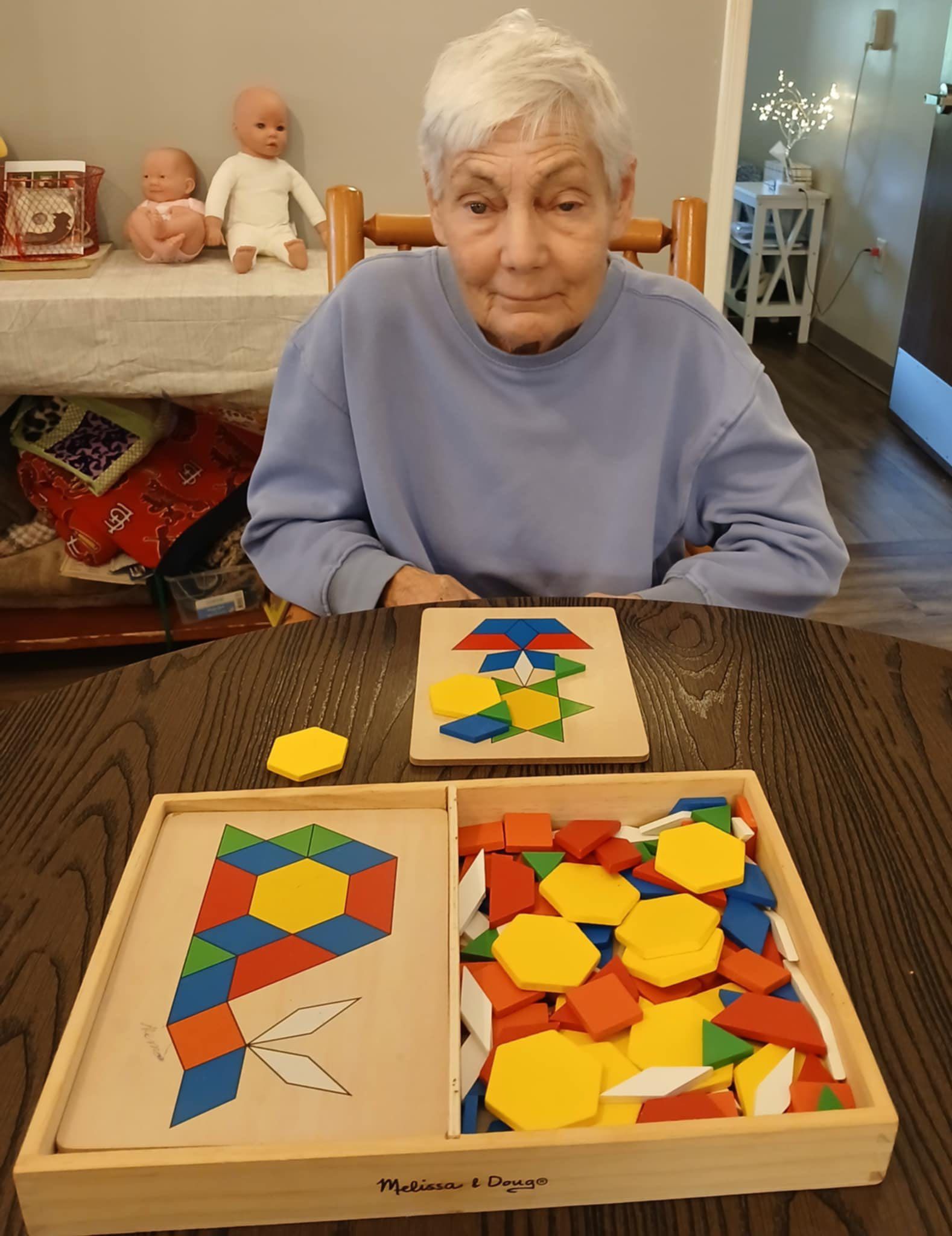 An elderly woman is sitting at a table playing with a wooden puzzle | fun at memory care home in ozark mo