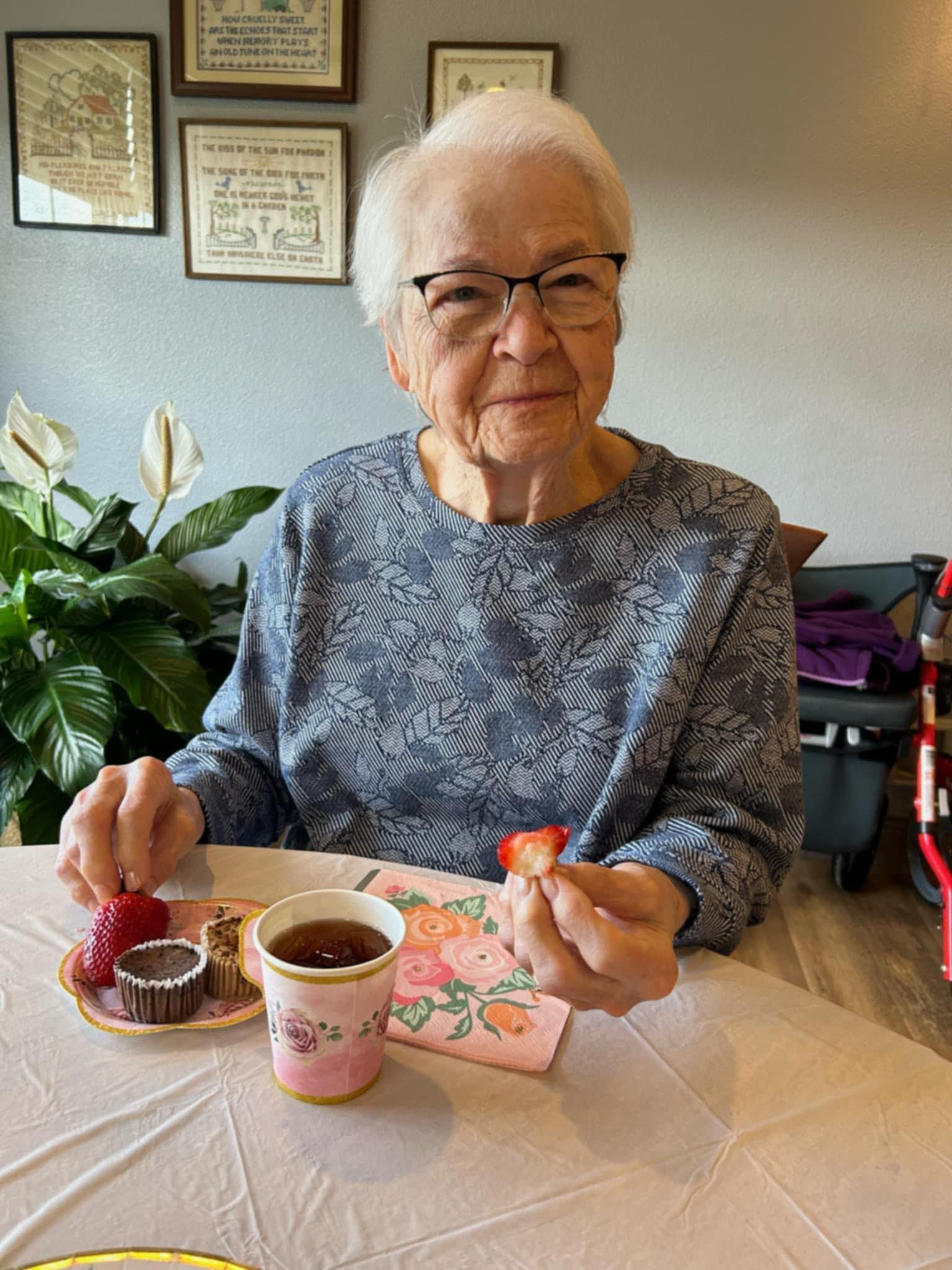 An elderly woman is sitting at a table eating strawberries and drinking tea.