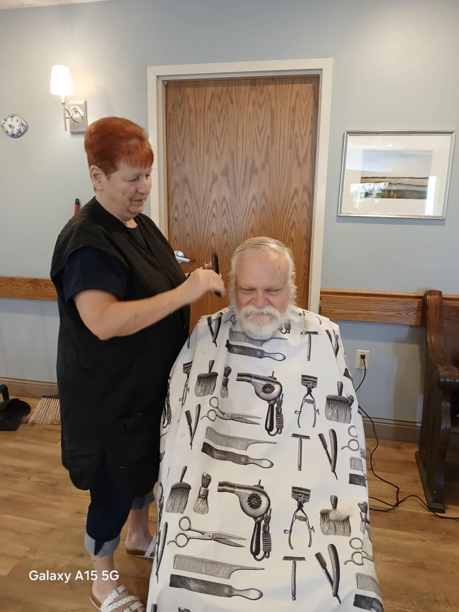 A man is getting his hair cut by a woman in a room.