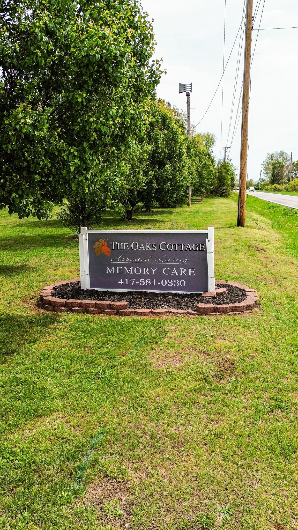 A sign is sitting in the middle of a grassy field next to a tree.