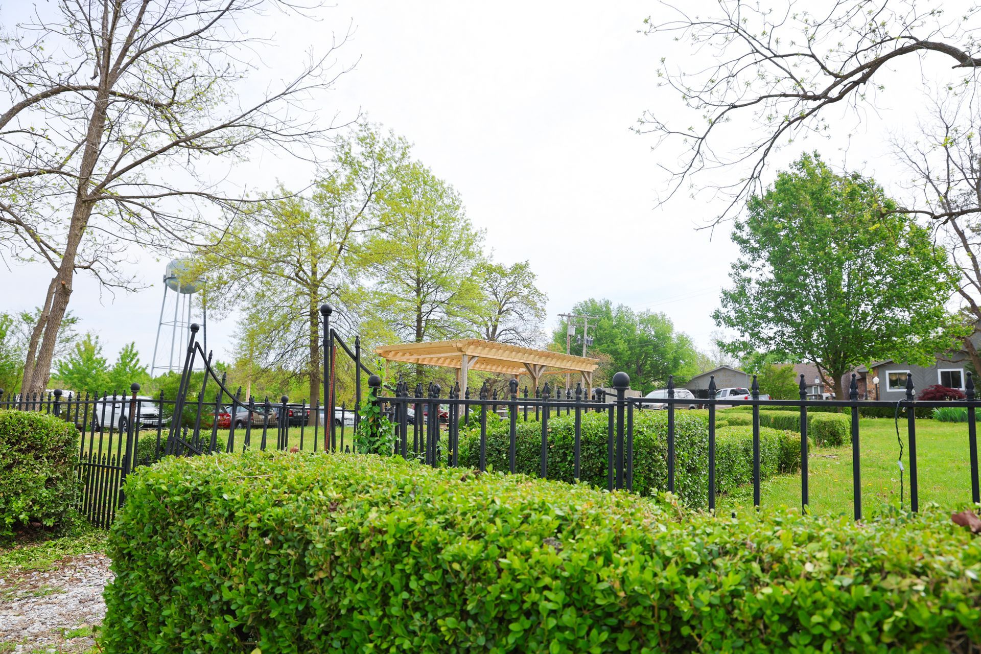A black fence surrounds a park with trees and bushes.