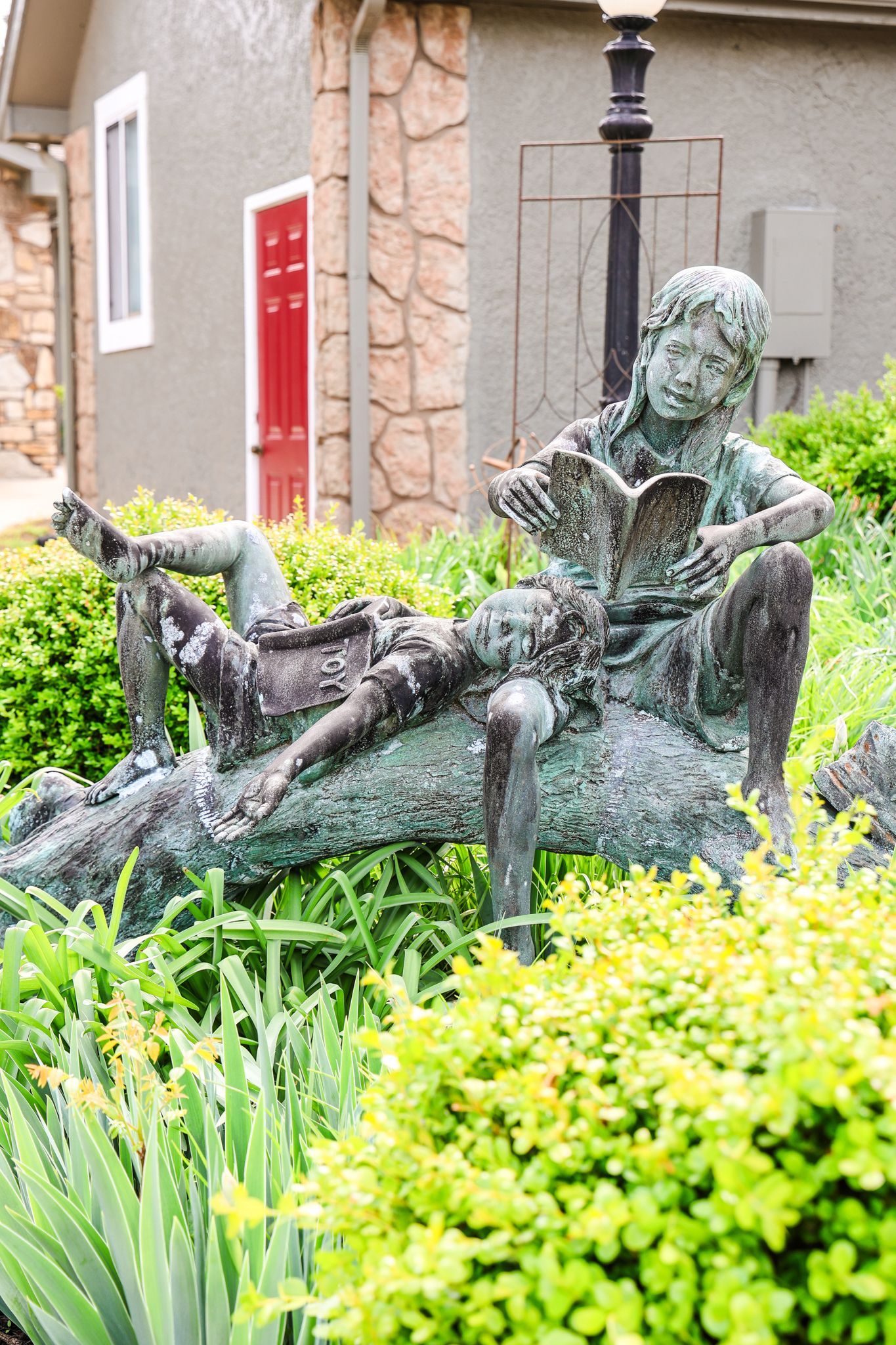 A statue of a boy sitting on a log reading a book.