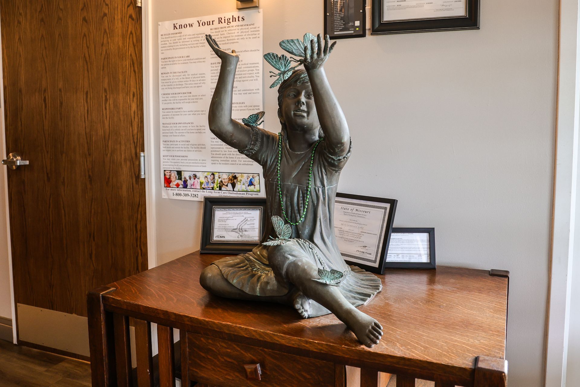 A statue of a woman sitting on a wooden table holding a dragonfly.