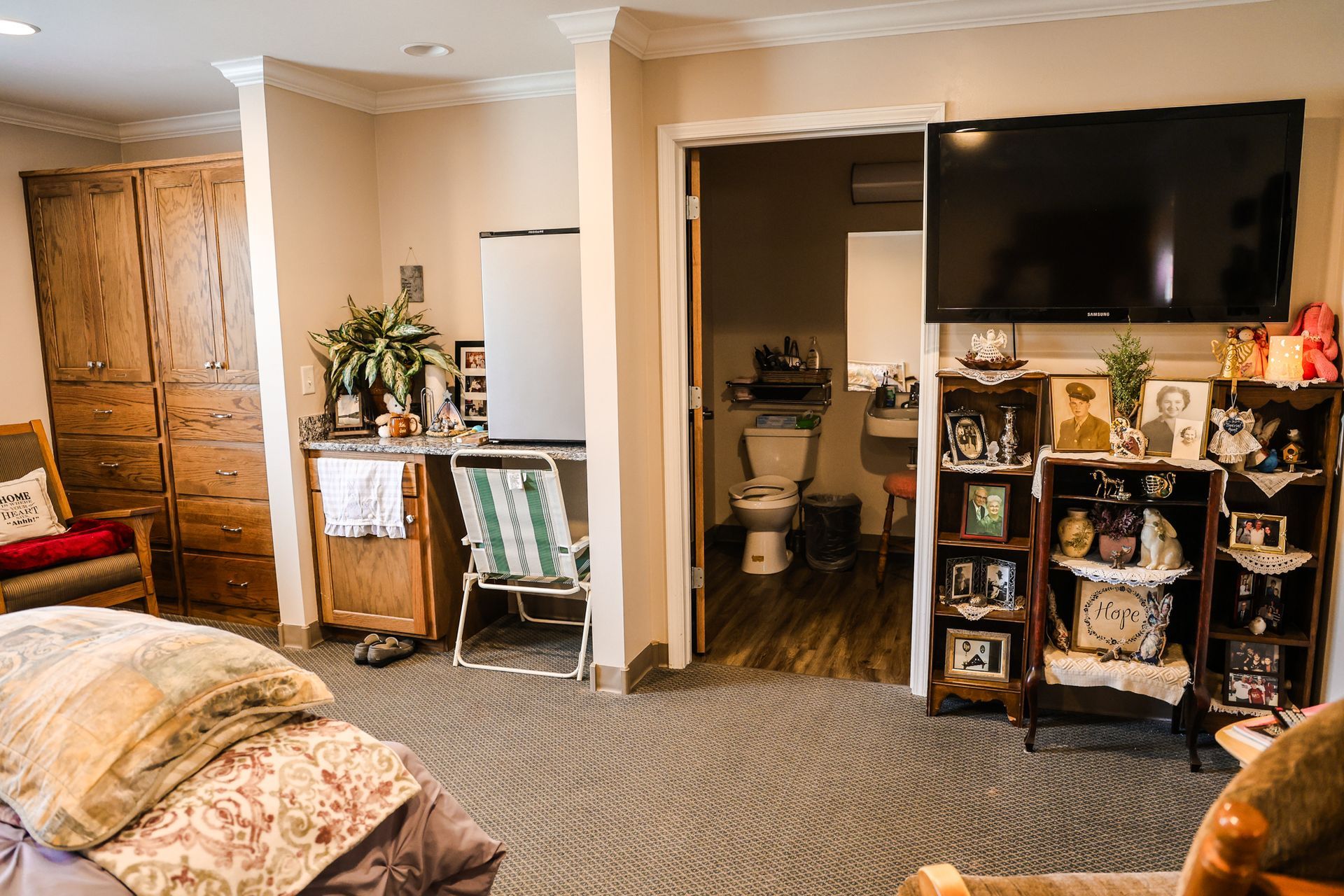 A living room with a bed , chairs , a television and a toilet.
