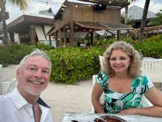 A man and a woman are sitting at a table on the beach.