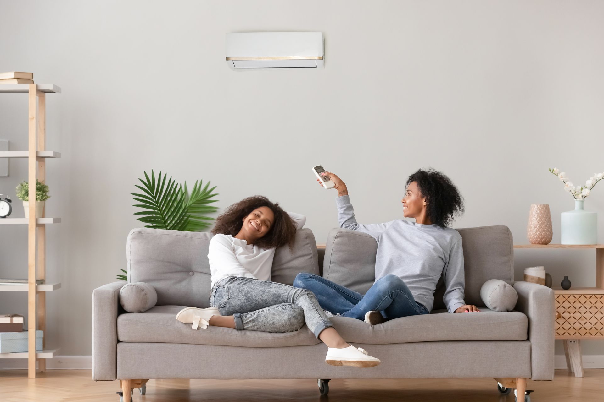 Two women are sitting on a couch in a living room holding remote controls.