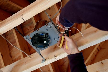 A person is working on a light fixture in the ceiling of a house.