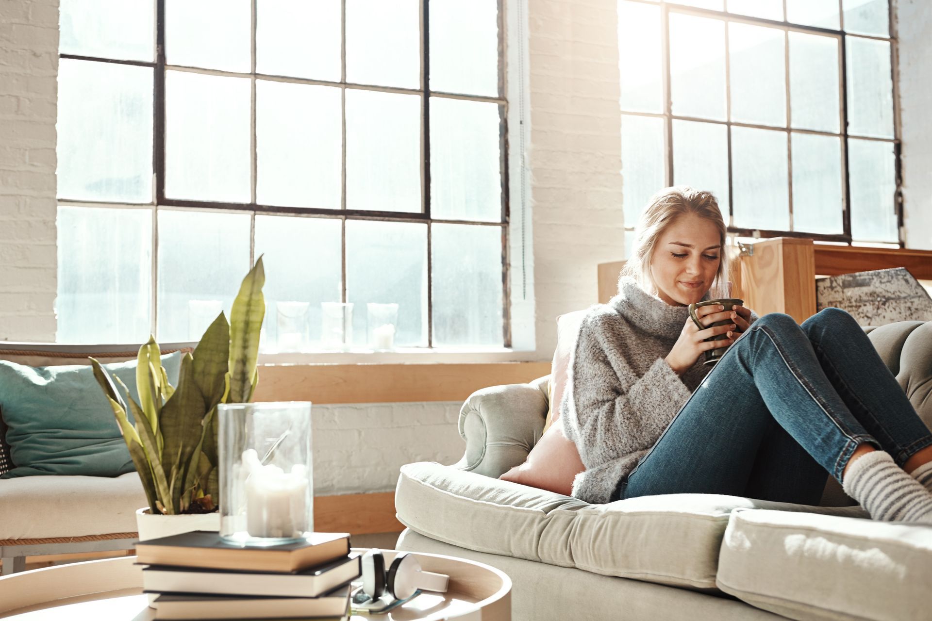 A woman is sitting on a couch holding a cup of coffee.