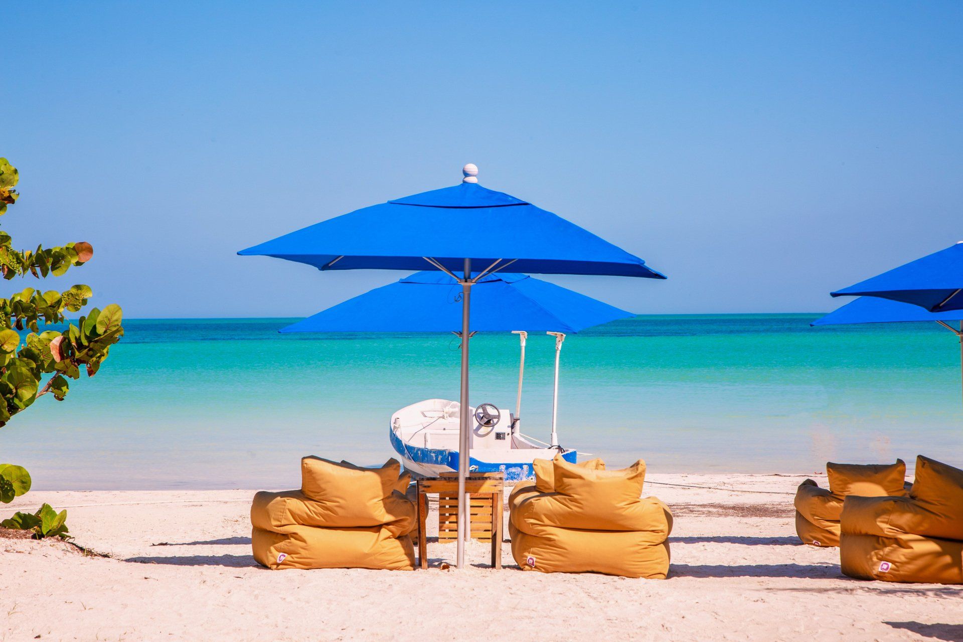 Una playa con sombrillas azules y un barco al fondo.