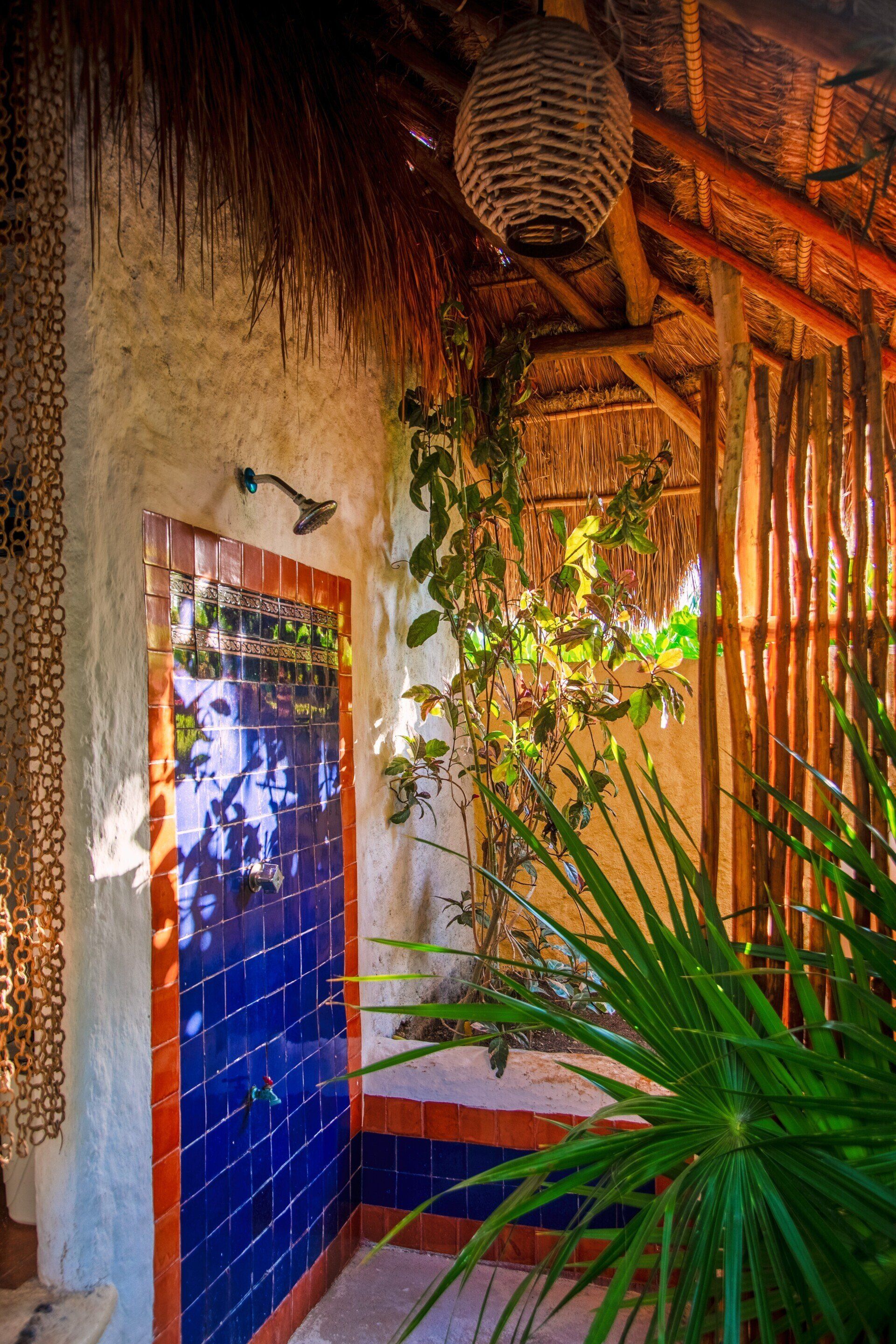 A bathroom with a shower and a thatched roof surrounded by plants.