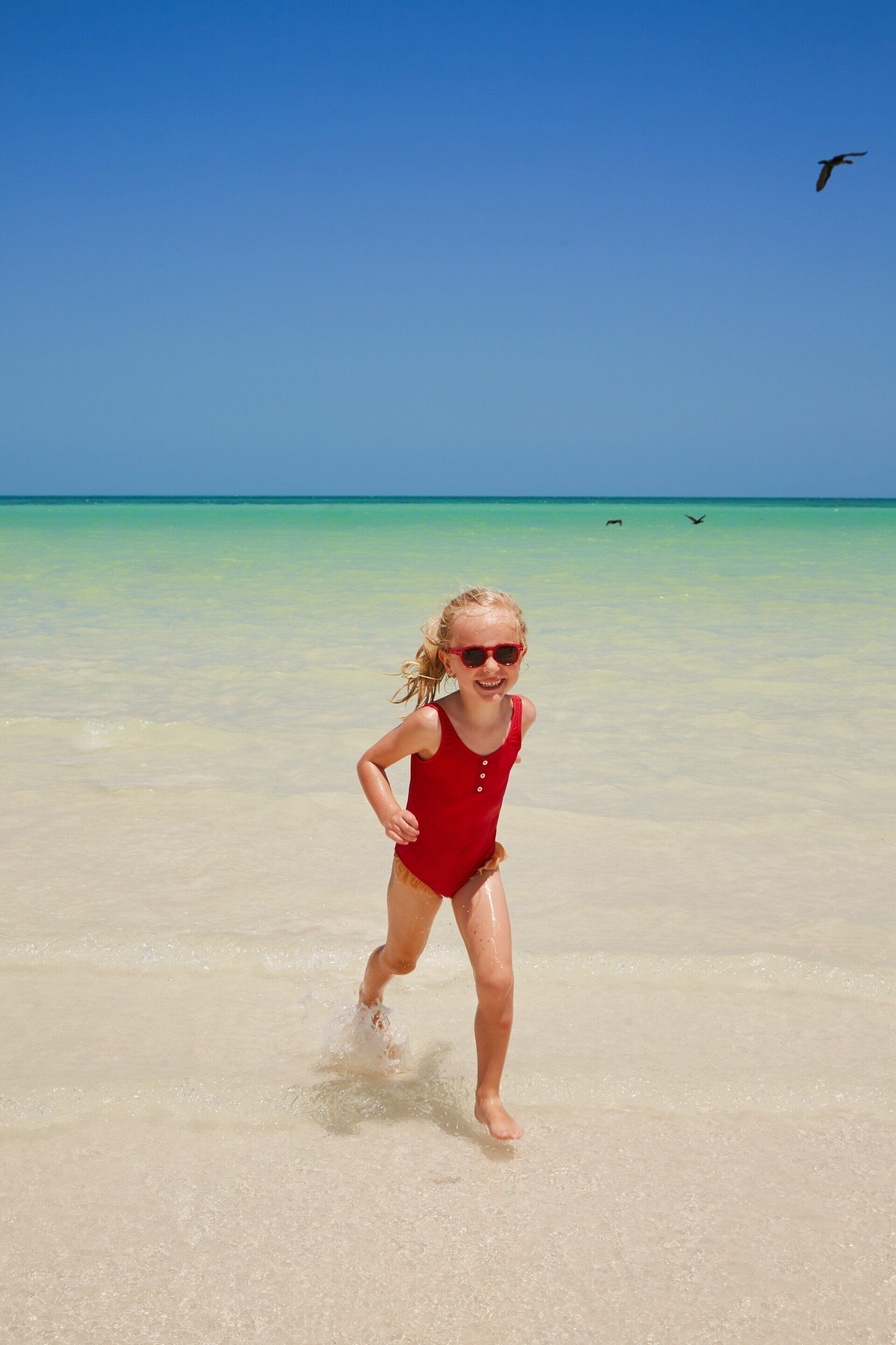 A little girl in a red swimsuit is running on the beach.