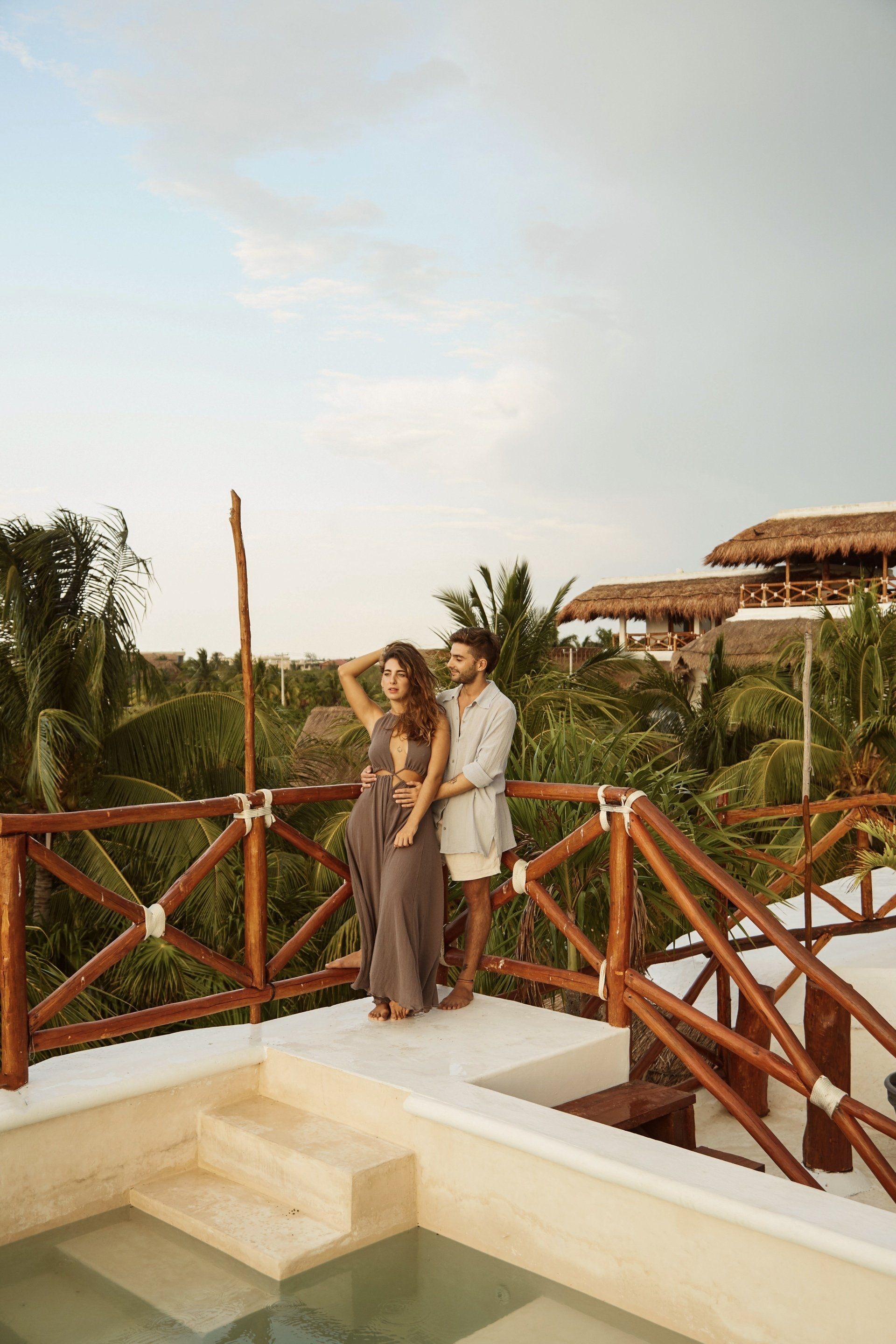 A man and a woman are standing on a balcony overlooking a swimming pool.