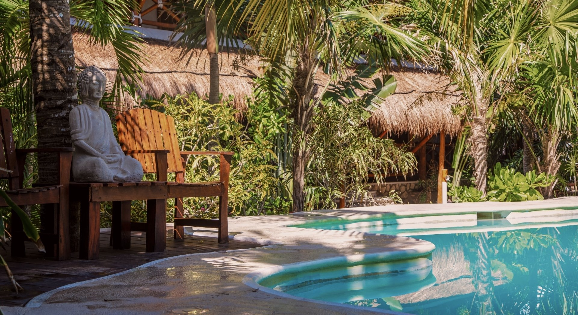 Una piscina  rodeada de pameras y una estatua de Buda