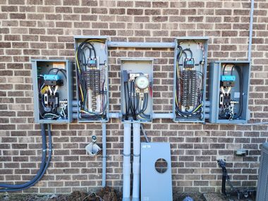 Electrical panel boxes mounted on a brick wall with conduits and a meter.
