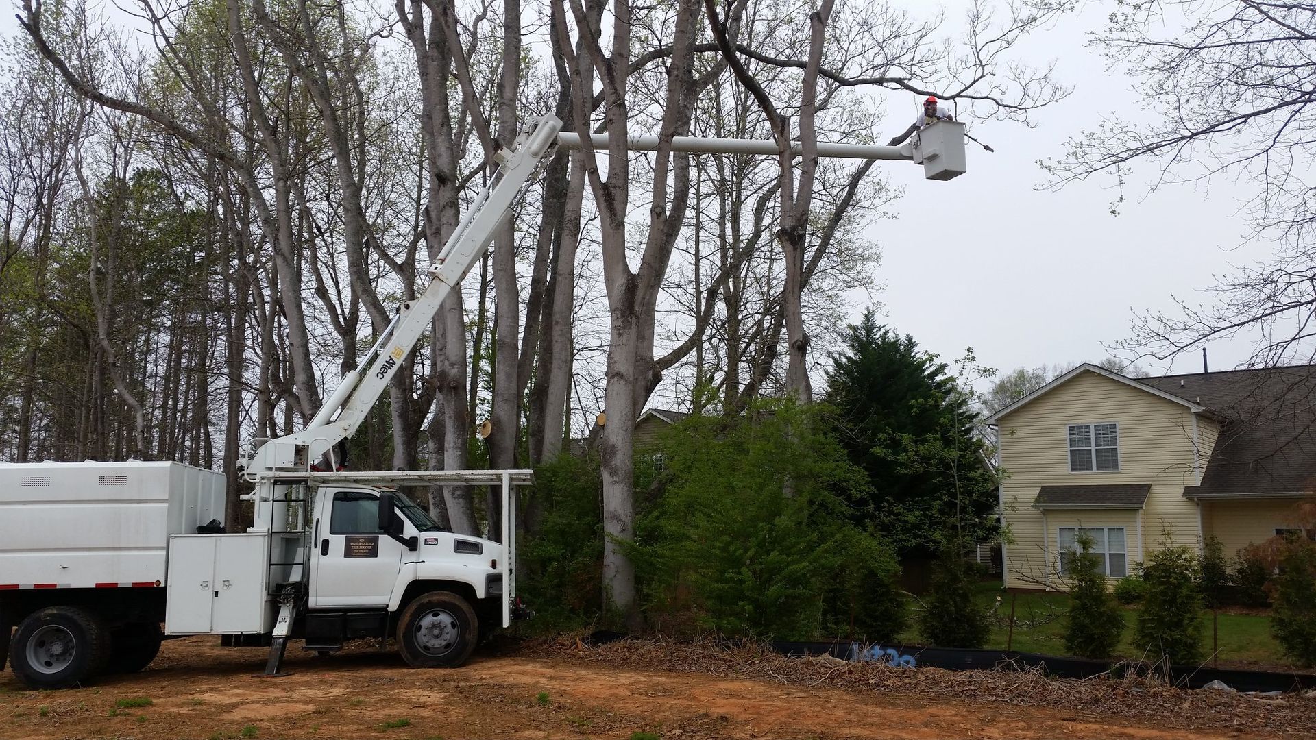 A white truck with a crane attached to it is parked in front of a house.