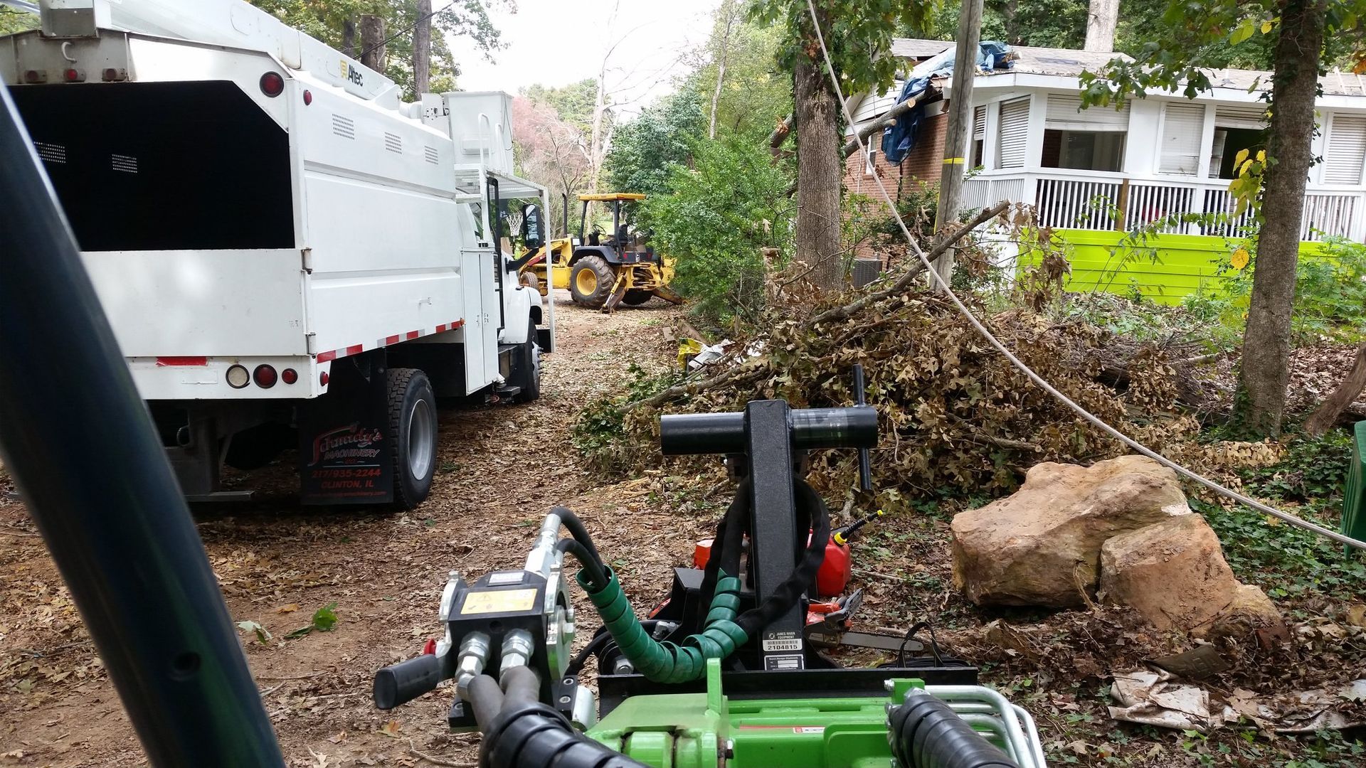 A white truck is parked next to a green machine in front of a house.