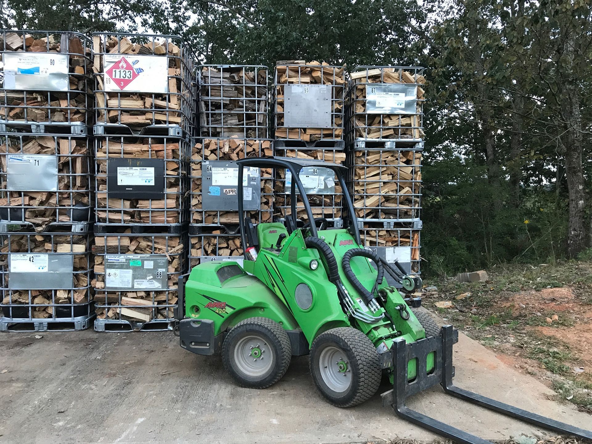 A green forklift is parked in front of a pile of logs.