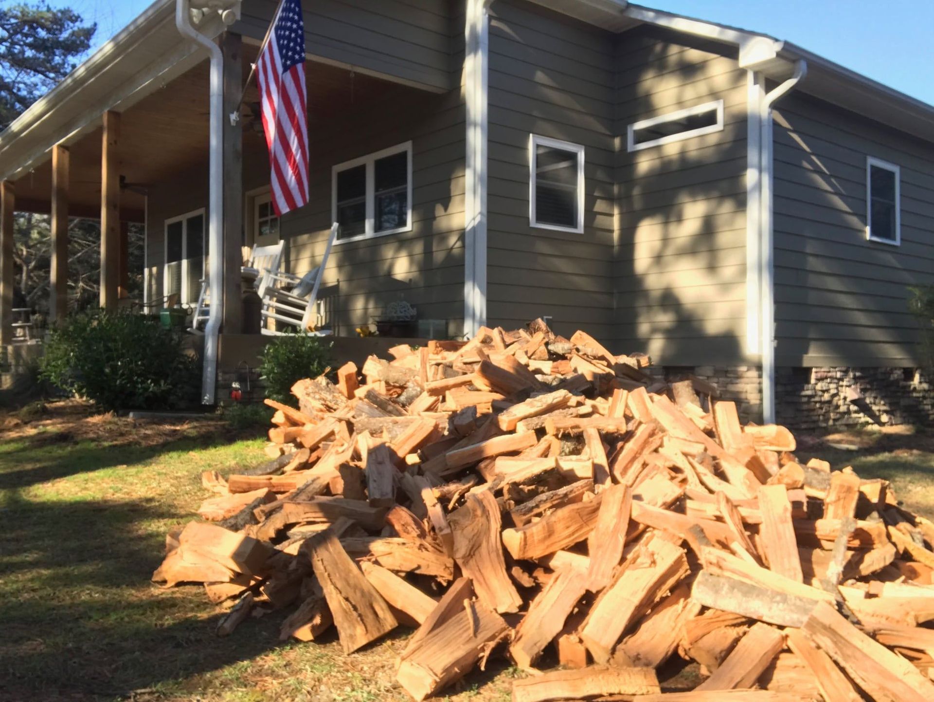 A large pile of wood is in front of a house