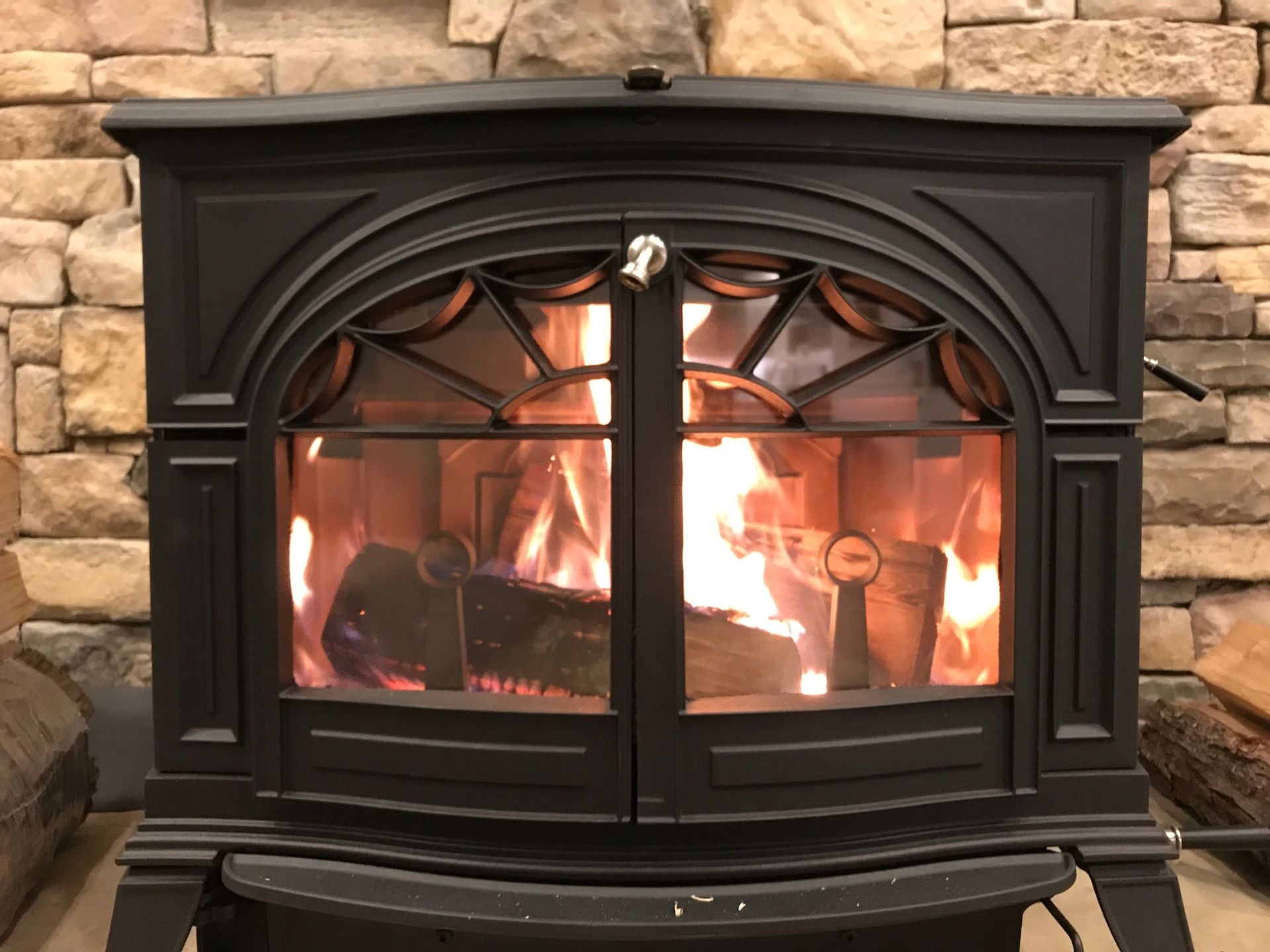 A black wood stove is sitting in front of a stone wall