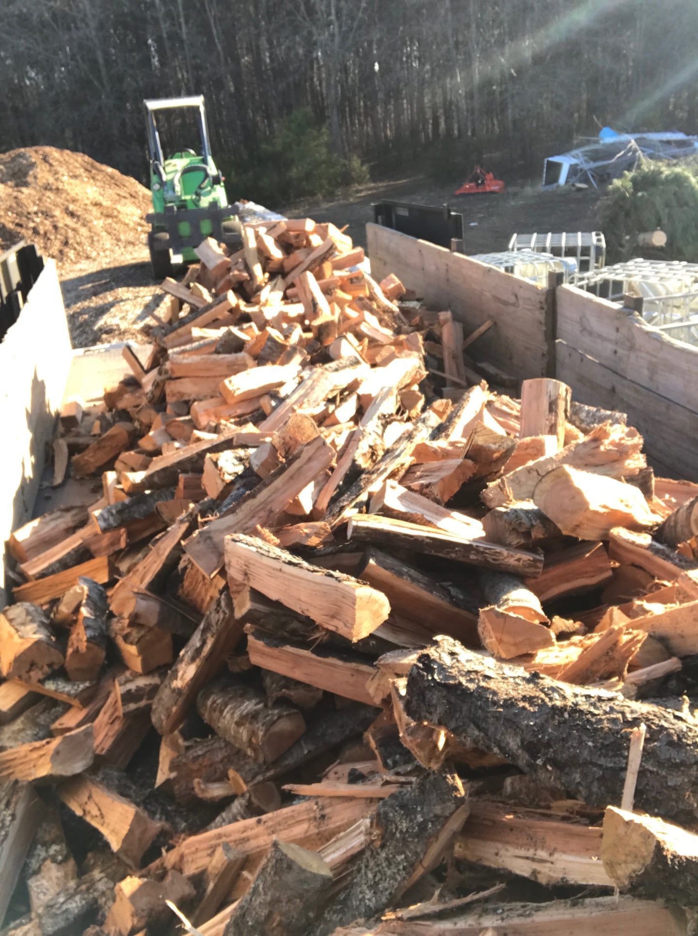 A pile of logs with a green forklift in the background