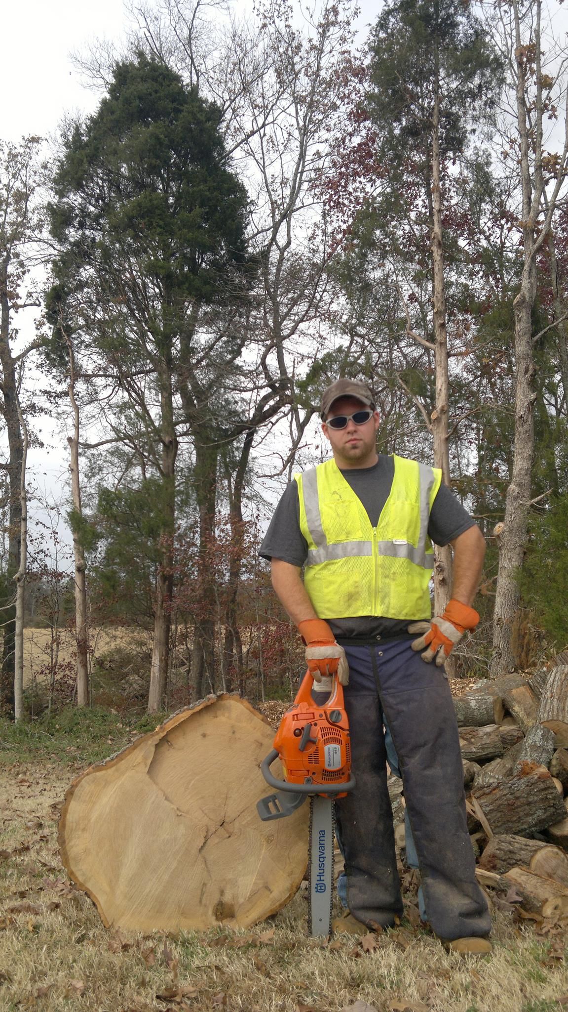 A man is standing next to a tree stump holding a chainsaw.