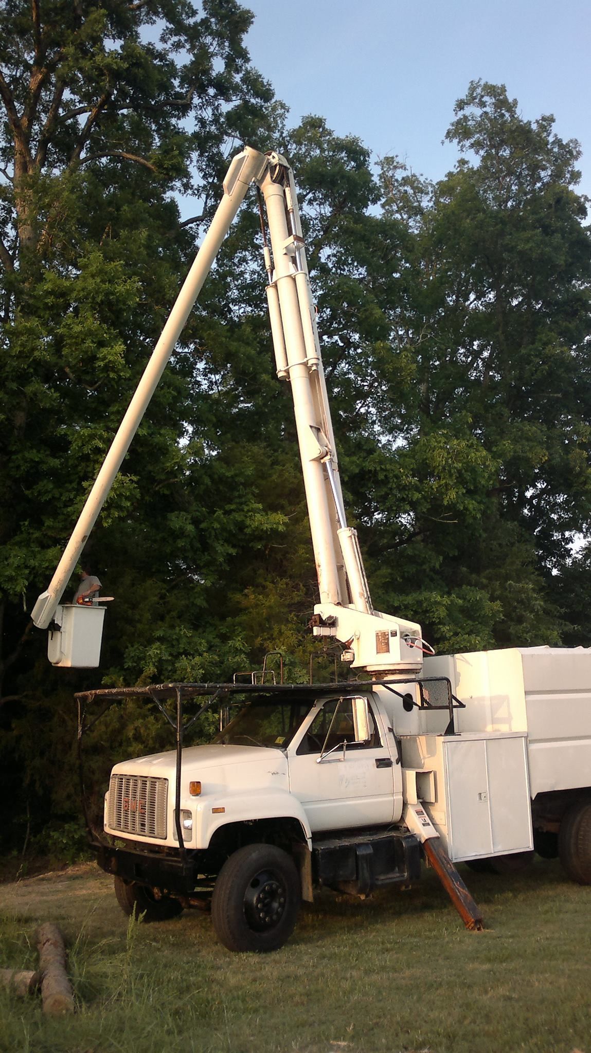 A white truck with a crane attached to it is parked in a grassy field.