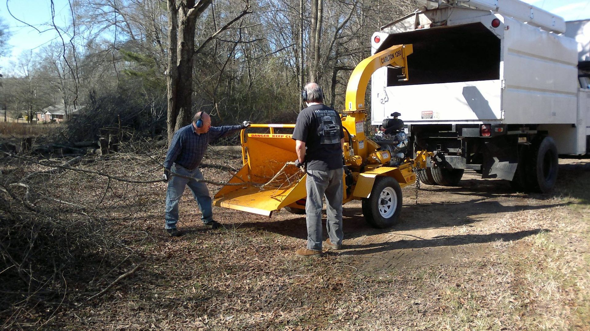 Two men are working on a tree chipper in front of a truck