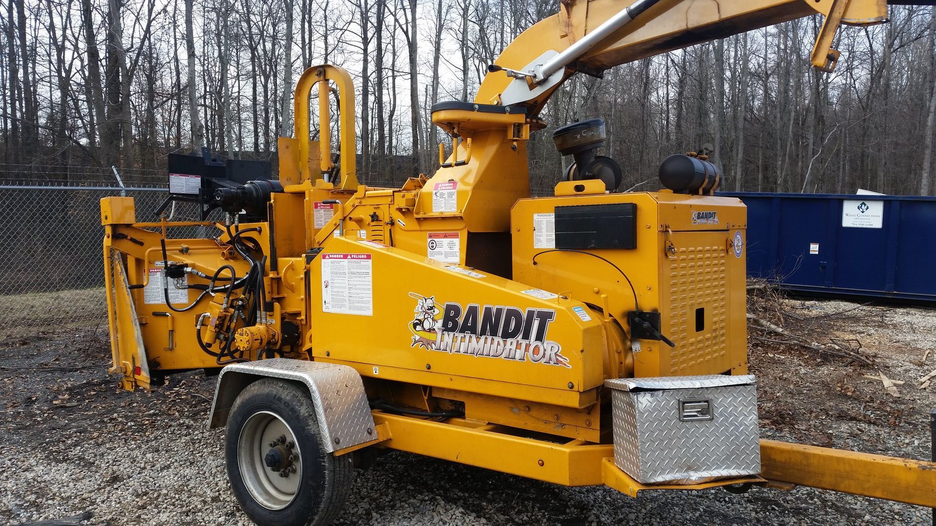 A yellow bandit wood chipper is parked in the dirt