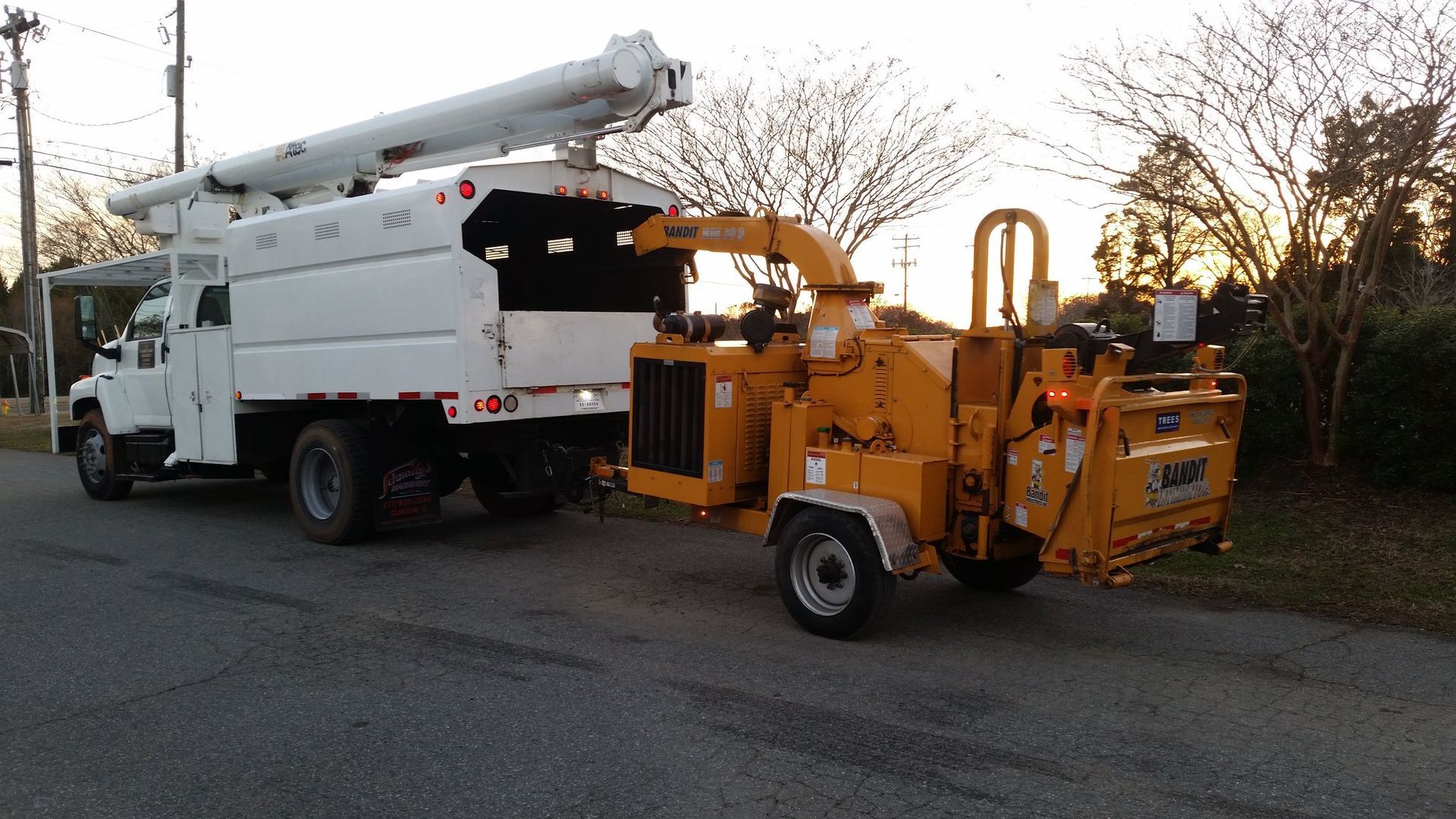 A tree chipper is attached to a white truck on the side of the road.