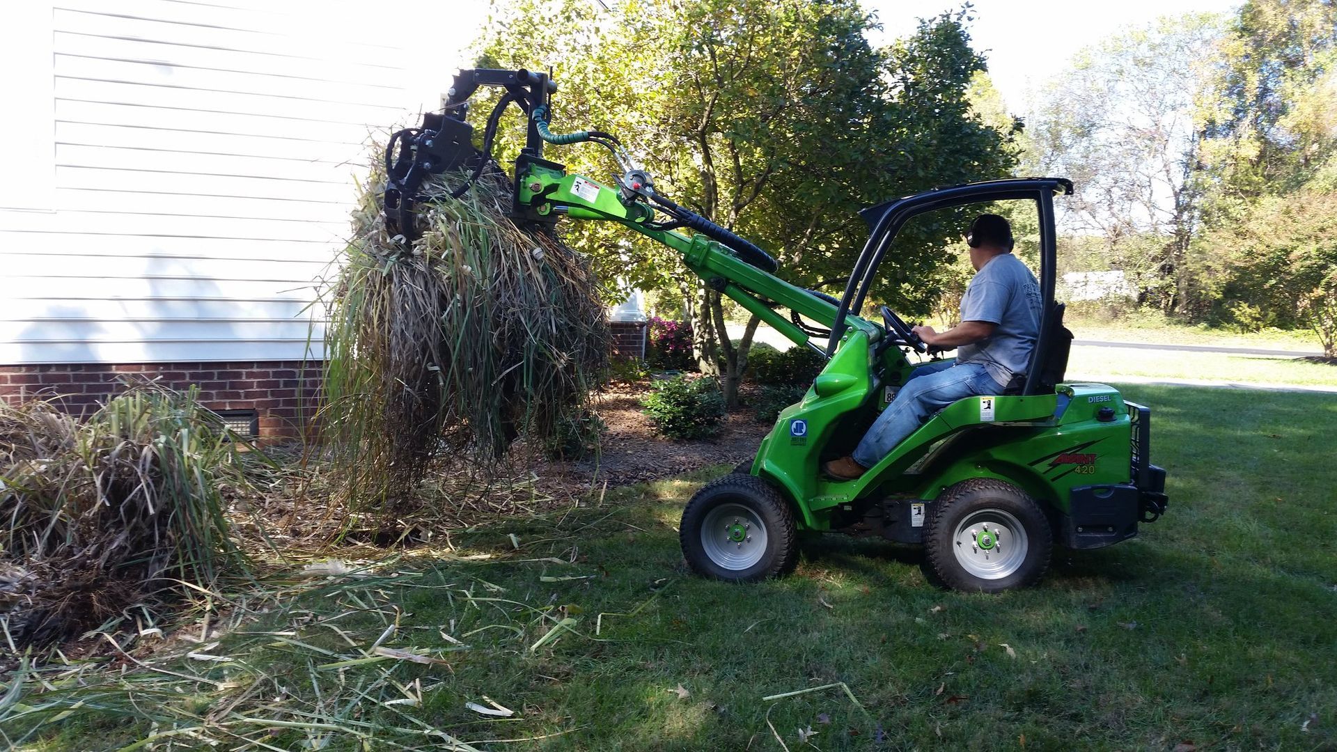 A man is driving a green tractor with a crane attached to it.
