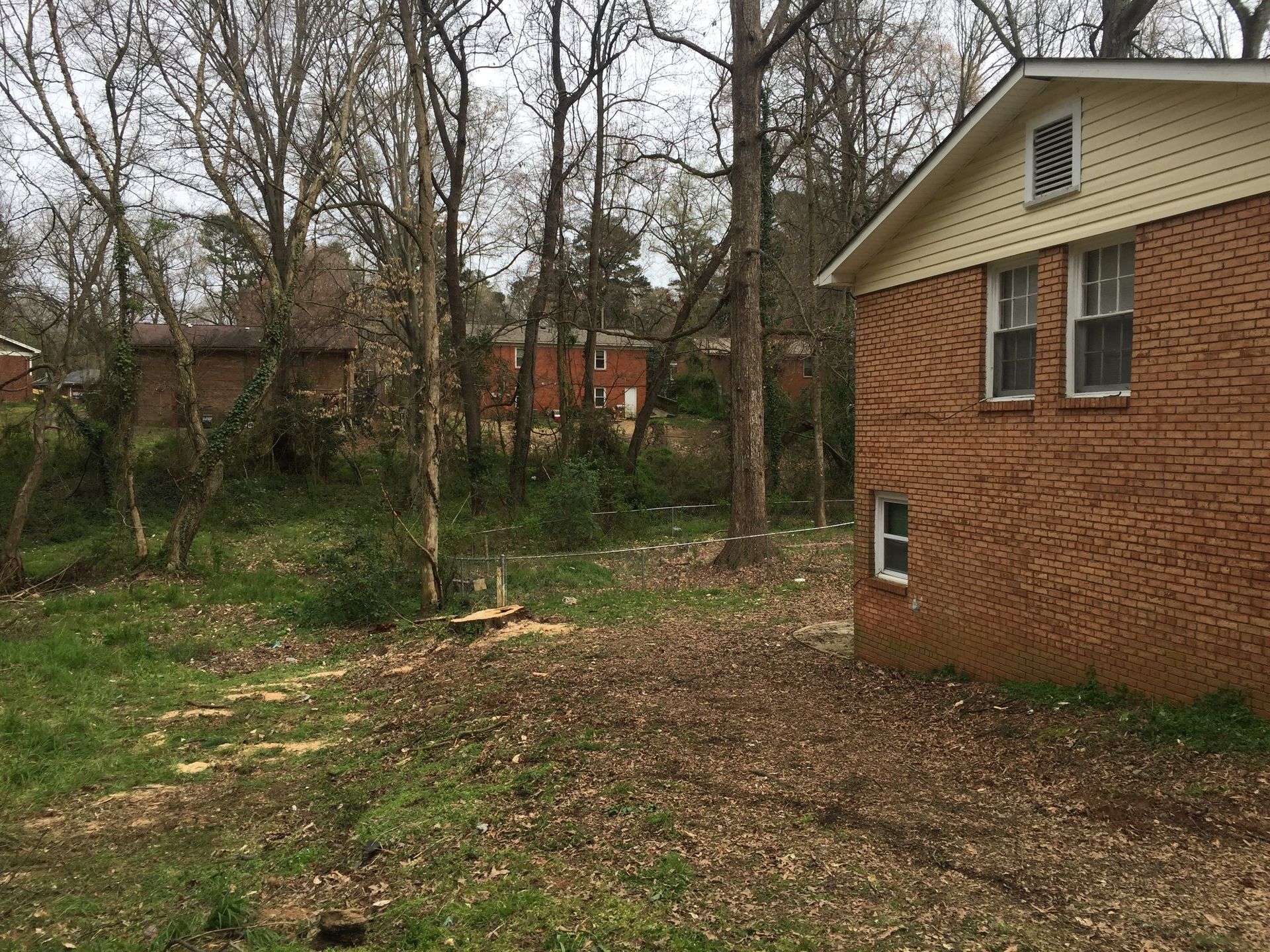 A brick house is sitting in the middle of a lush green field surrounded by trees.