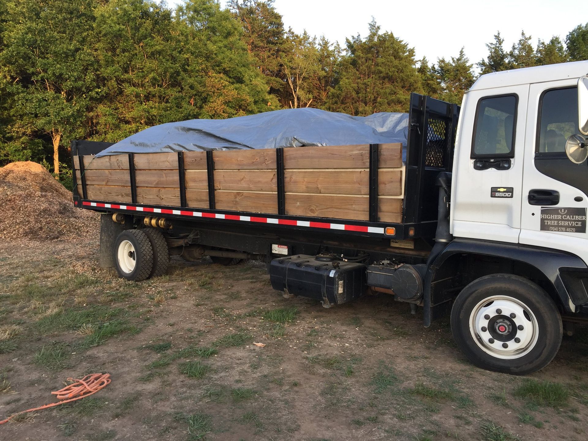 A white dump truck with a wooden bed is parked in a field.