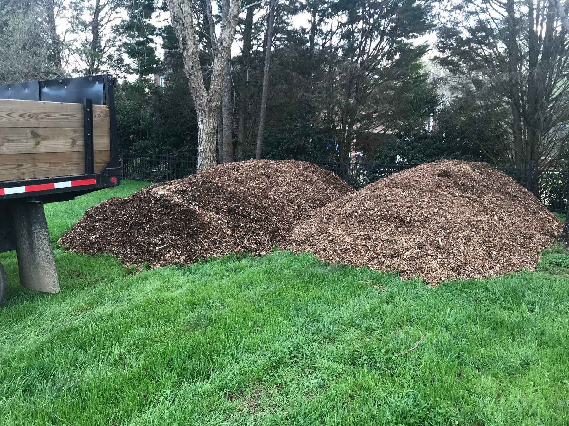 A pile of mulch is sitting in the grass next to a trailer.