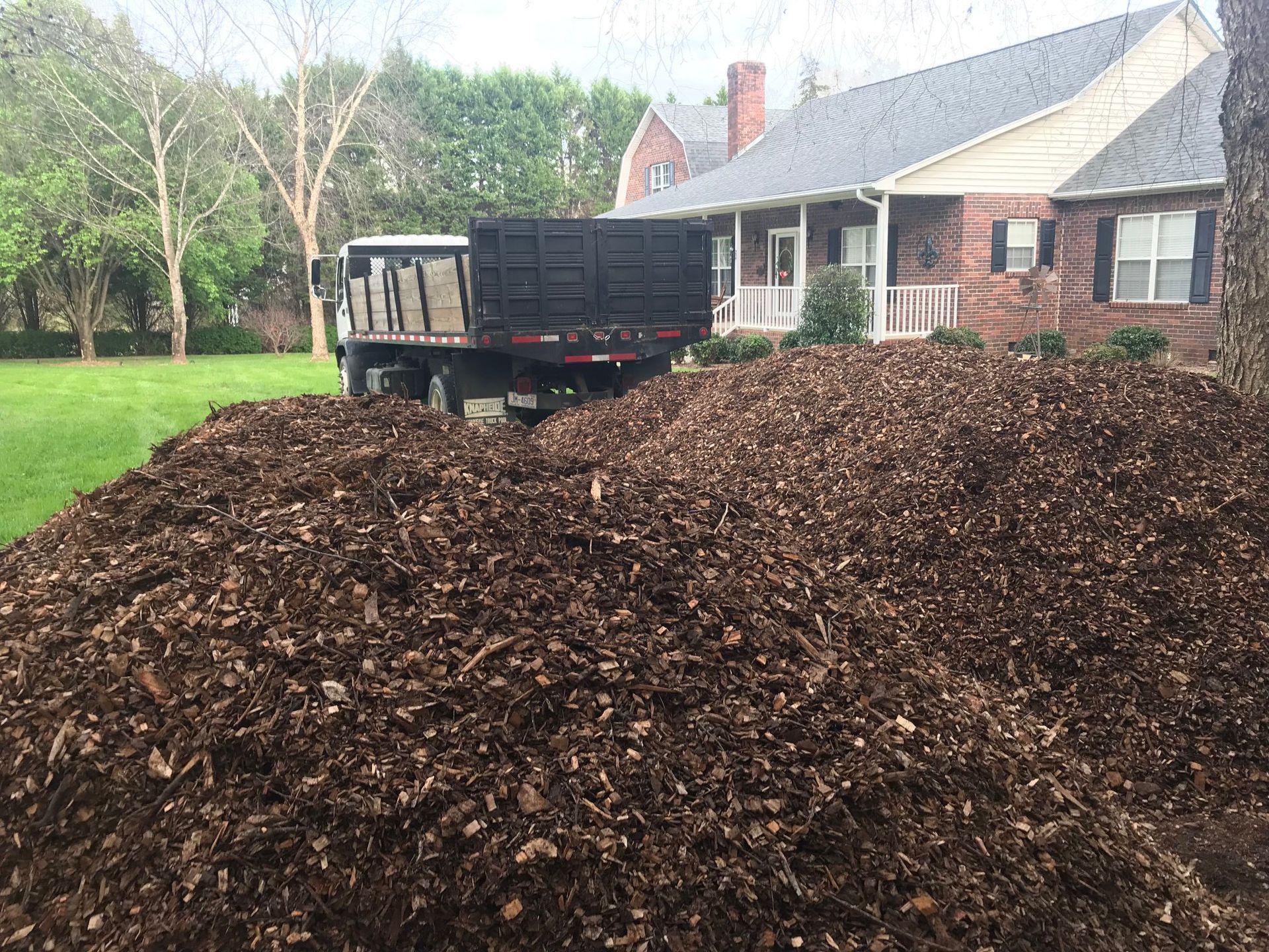 A dump truck is parked next to a pile of mulch in front of a house.