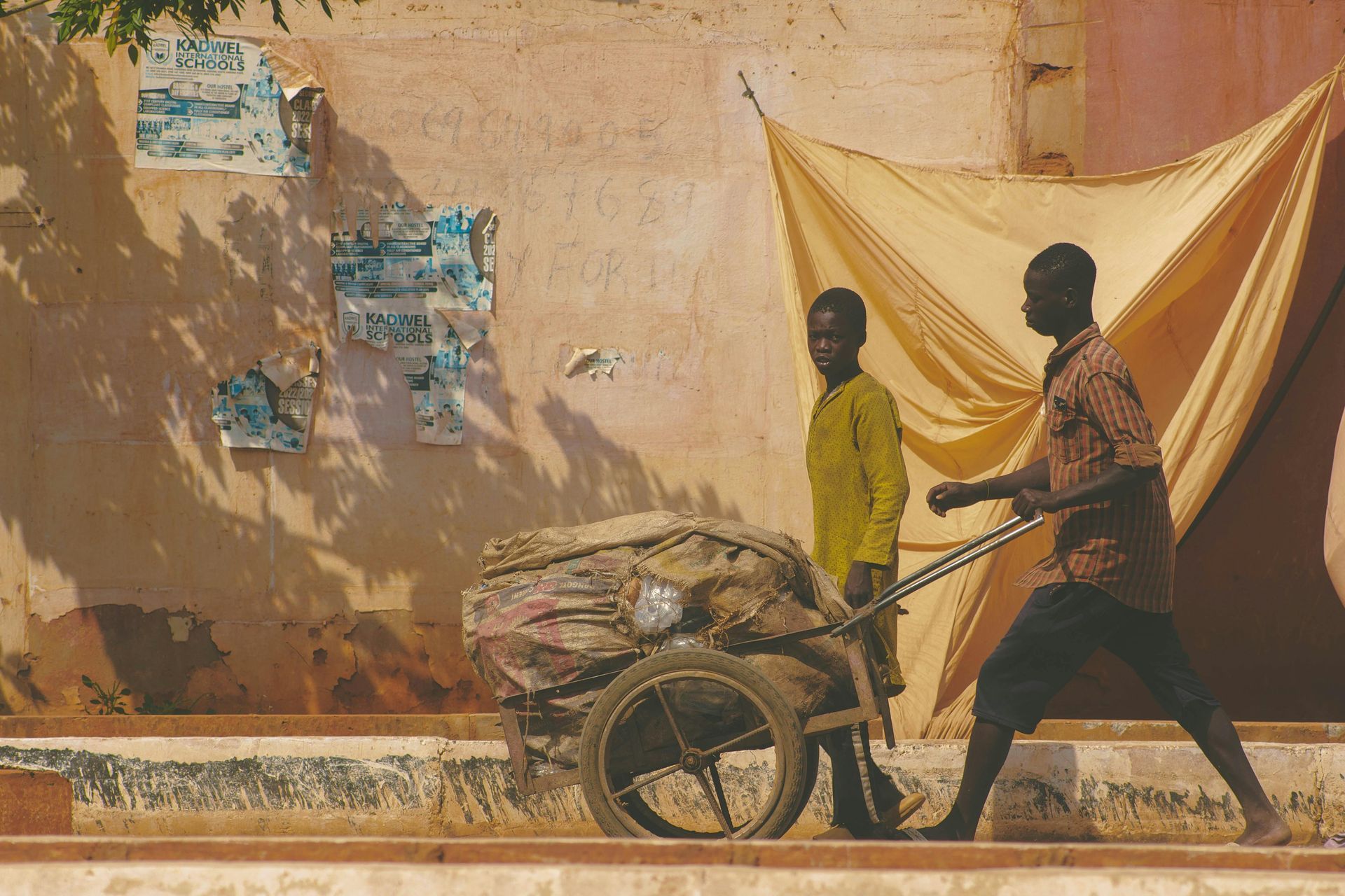 A man pushing a wheelbarrow with another man standing behind him