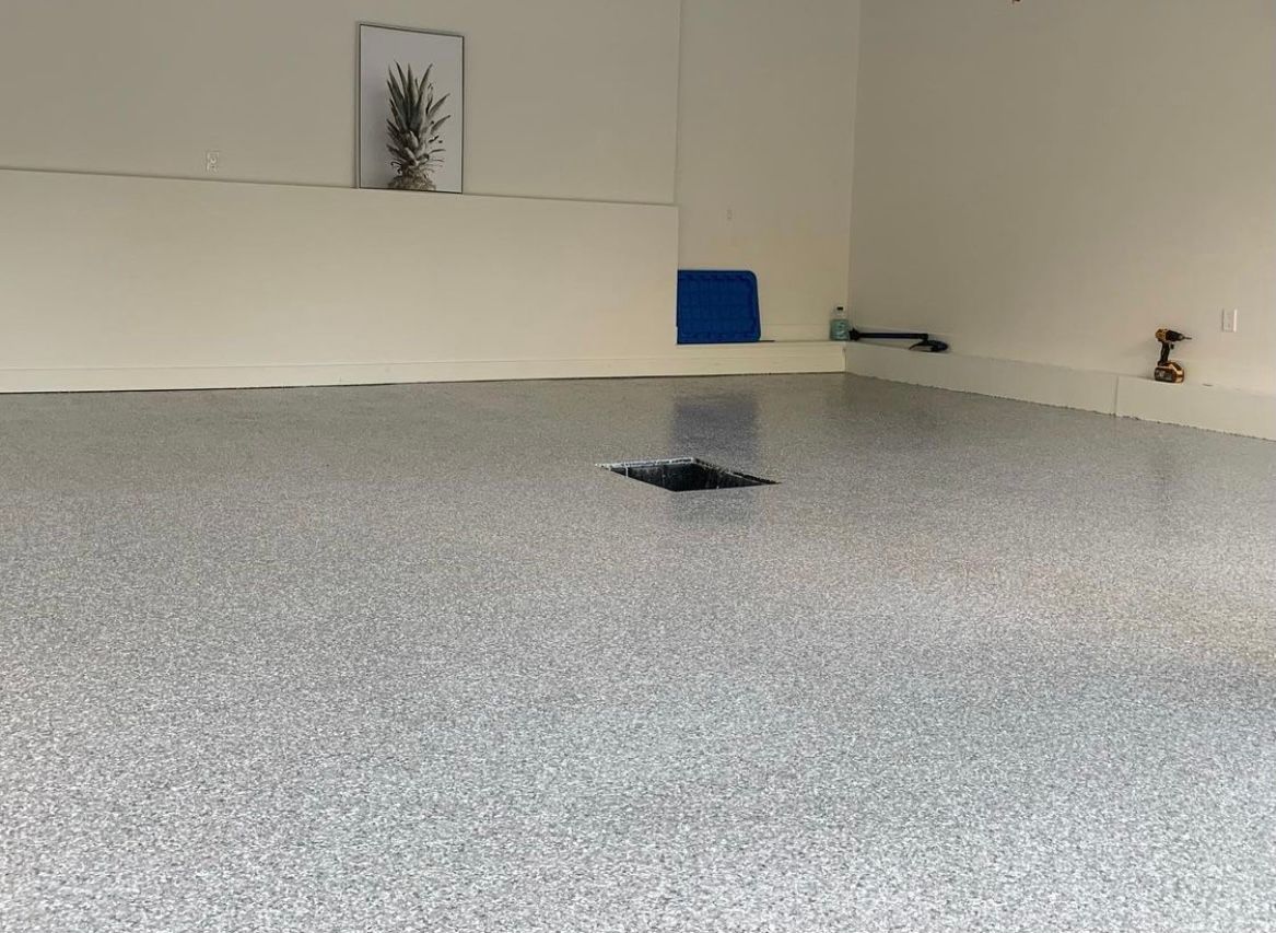 A garage floor with a hole in it and a picture on the wall.