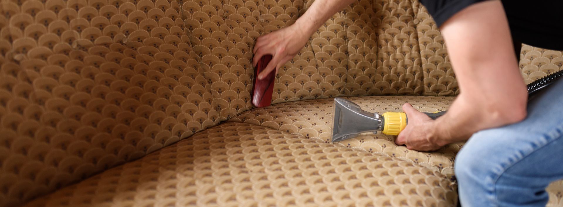 A man is cleaning a couch with a vacuum cleaner.