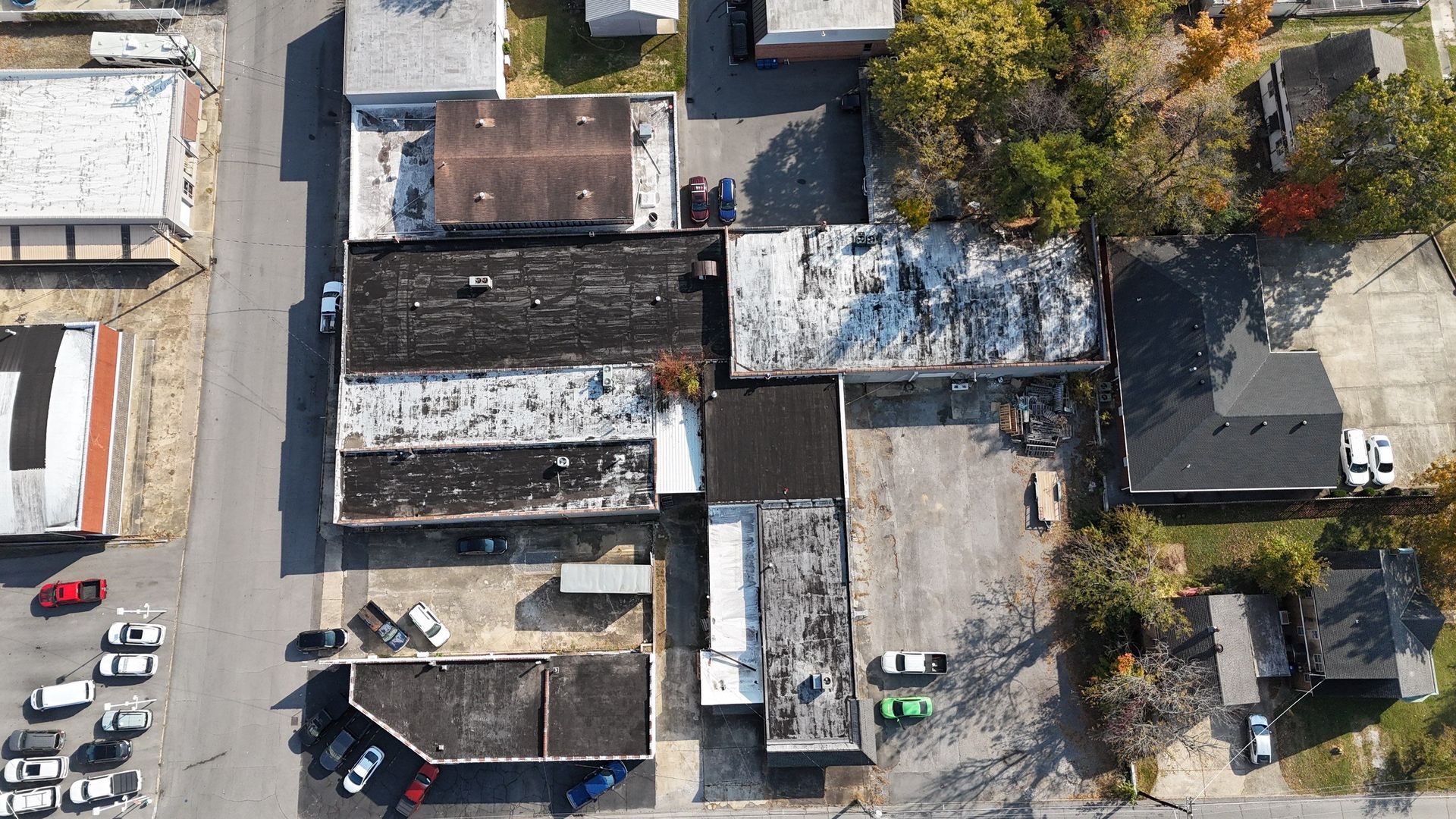 Aerial view of a row of rooftops, parked cars, and trees along a street.