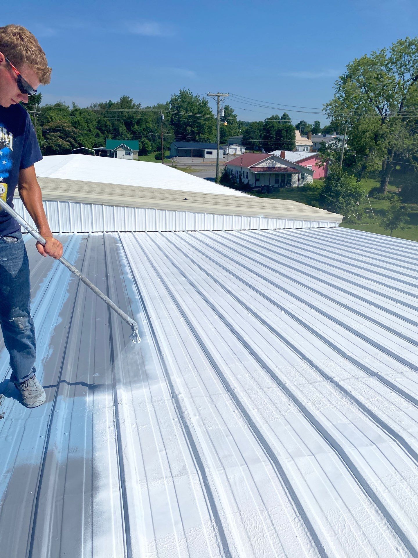 A man is painting a metal roof with a sprayer.