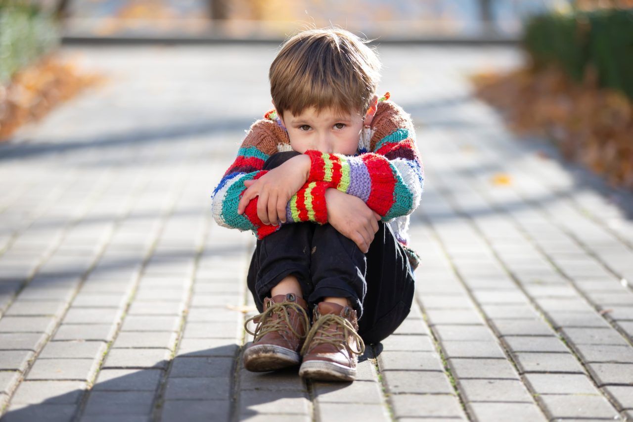sad little boy sitting alone in a park